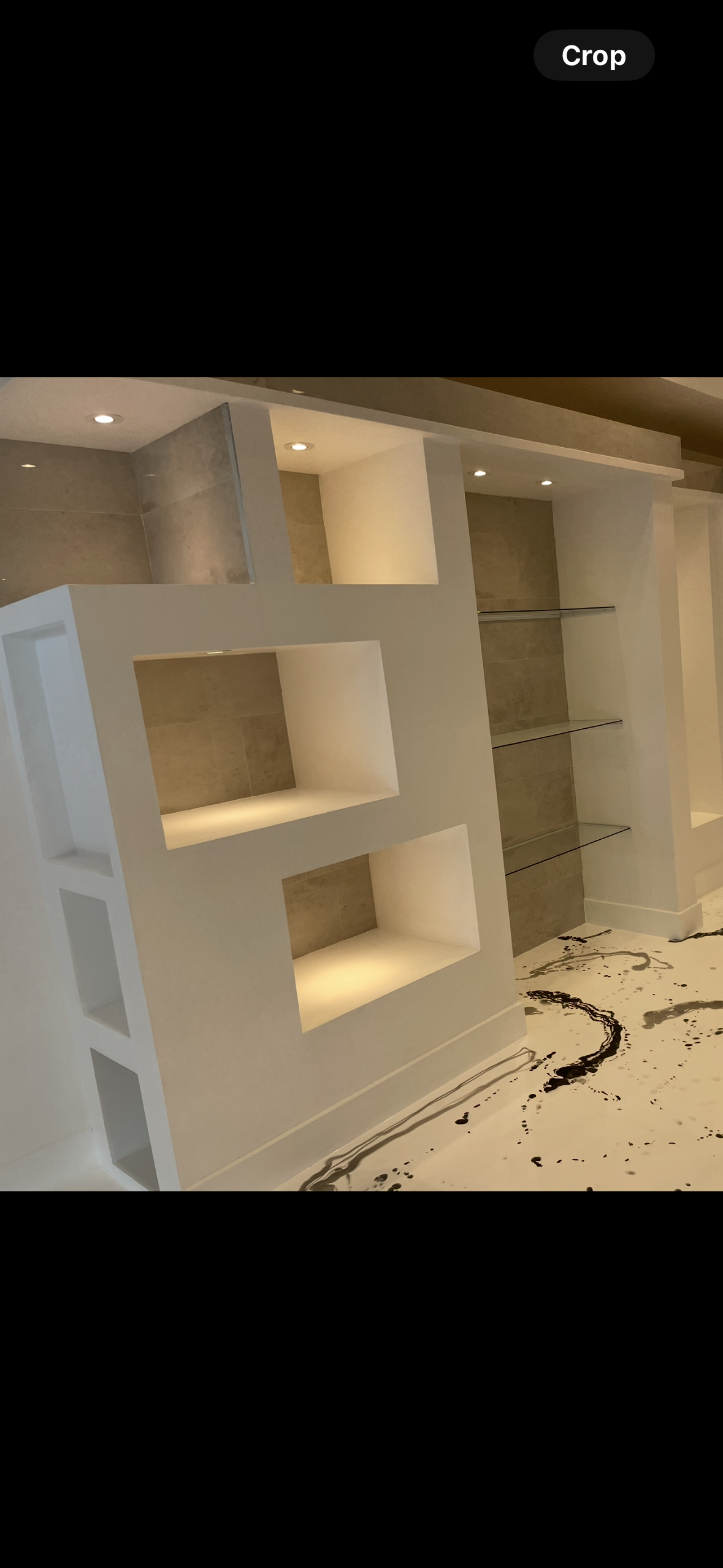 Interior featuring white built-in shelving unit with illuminated cubby holes, a wall with glass shelves, and marble flooring with black and gray veining. Peachtree city Ga.