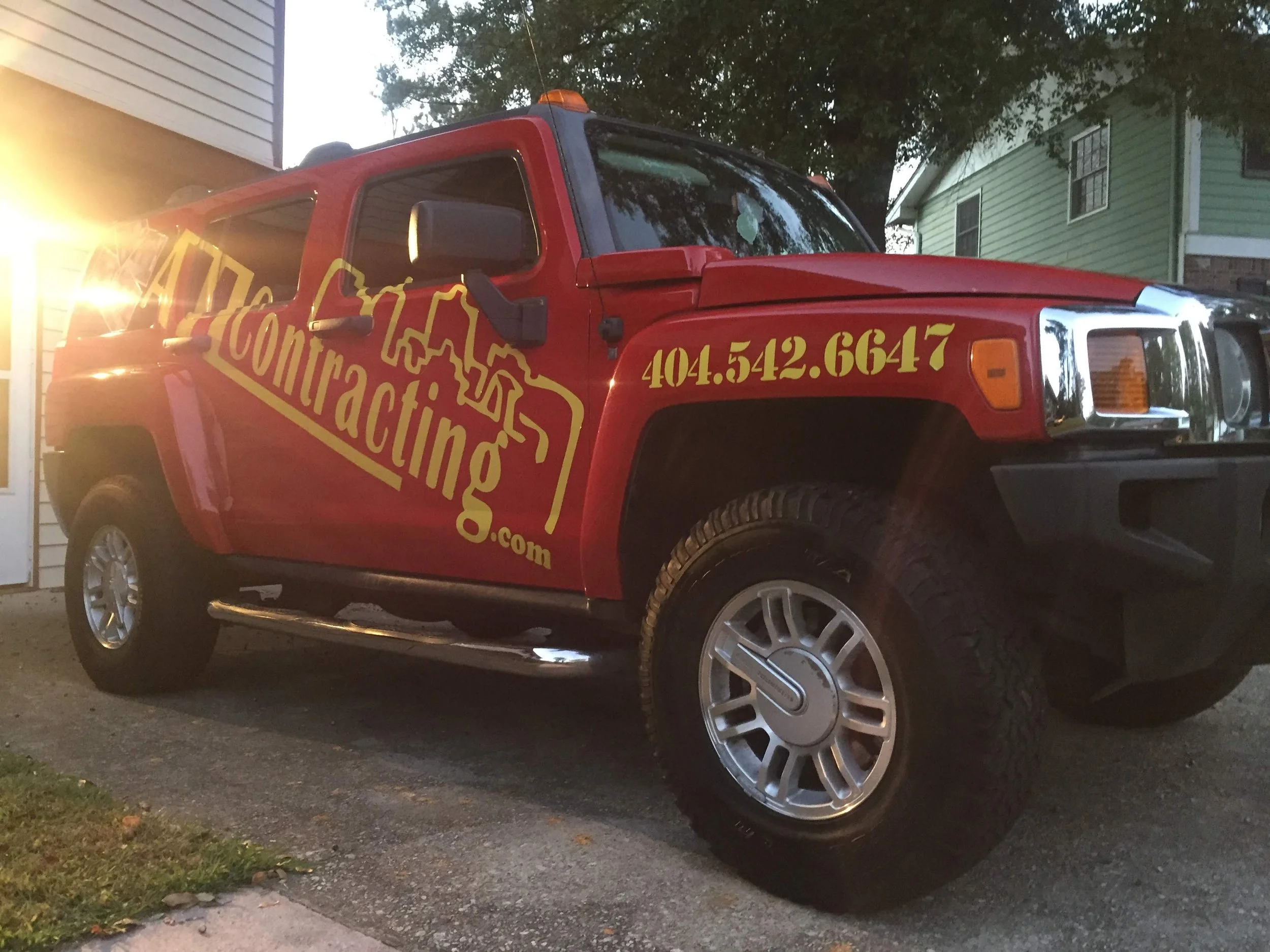 Red hummer displaying the company ATL Basement Solutions and Atl contracting parked on a driveway in front of houses, with large silver rims and a yellow logo or text on the side. Stockbridge ga.