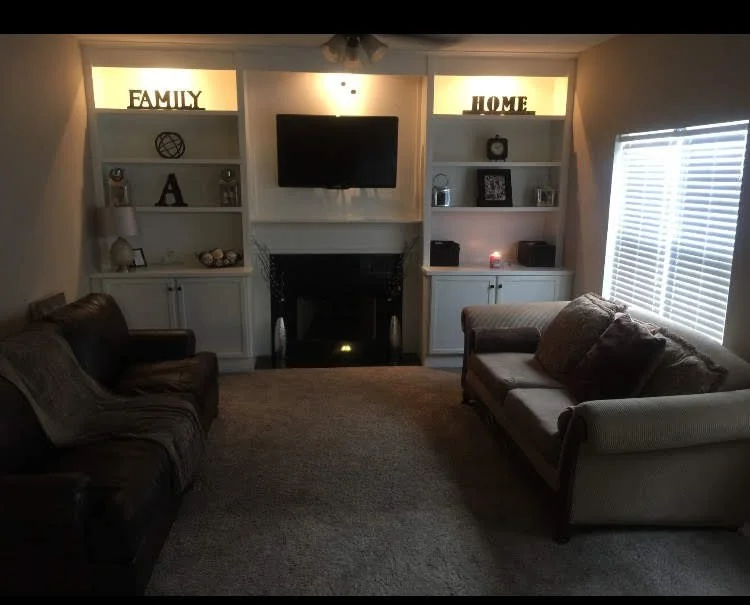 Custom  built-in TV fireplace unit with shelves and cabinets, decorative items, and a large window with blinds on the right side. Riverdale Ga.