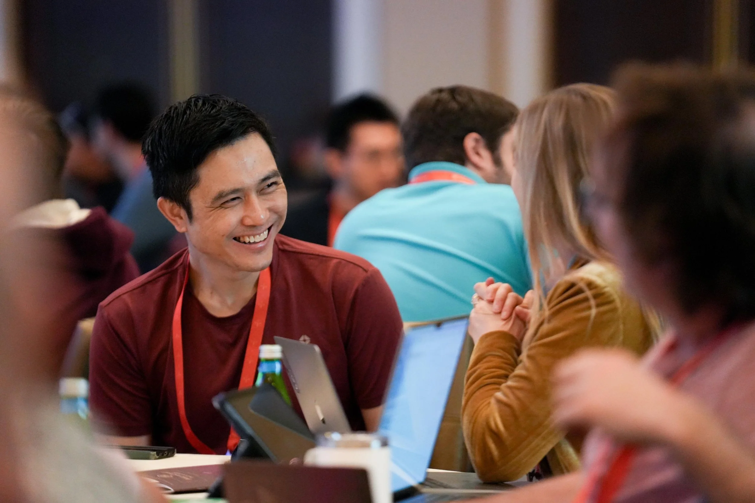 A group of people sitting at a table engaged in conversation, with one man smiling warmly.