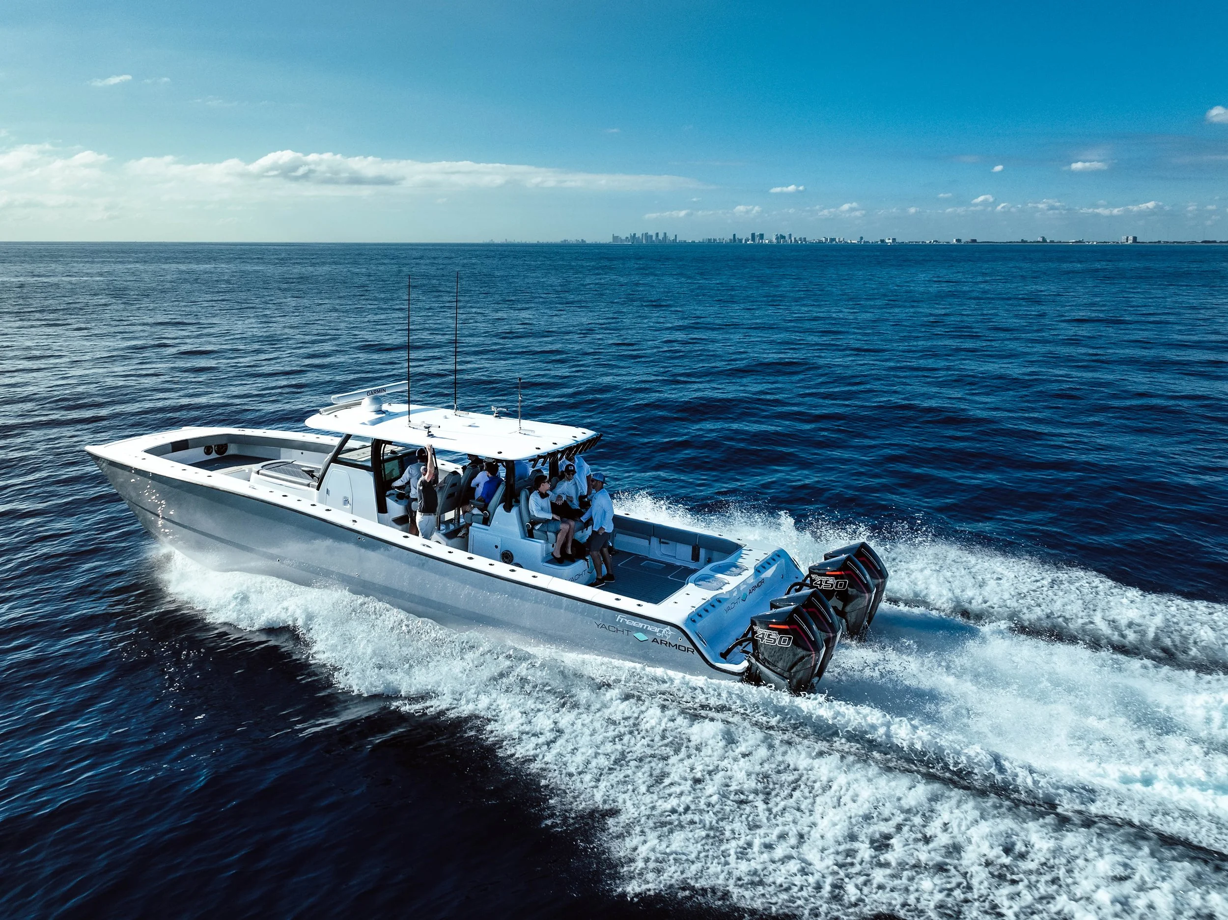 A group of people riding on a white speedboat on open water with a distant city skyline in the background.