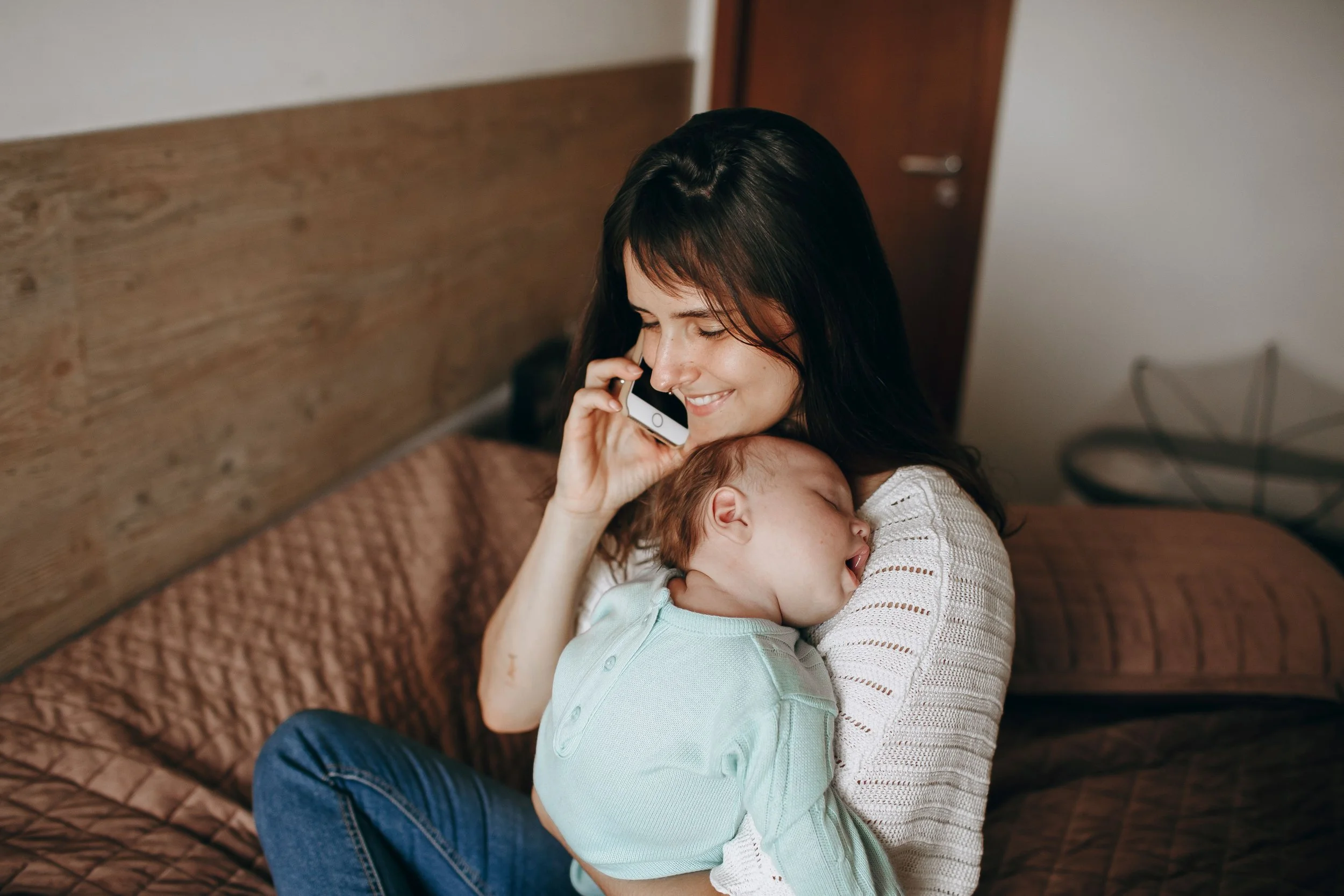 Mom smiling while talking on phone while holding sleeping baby