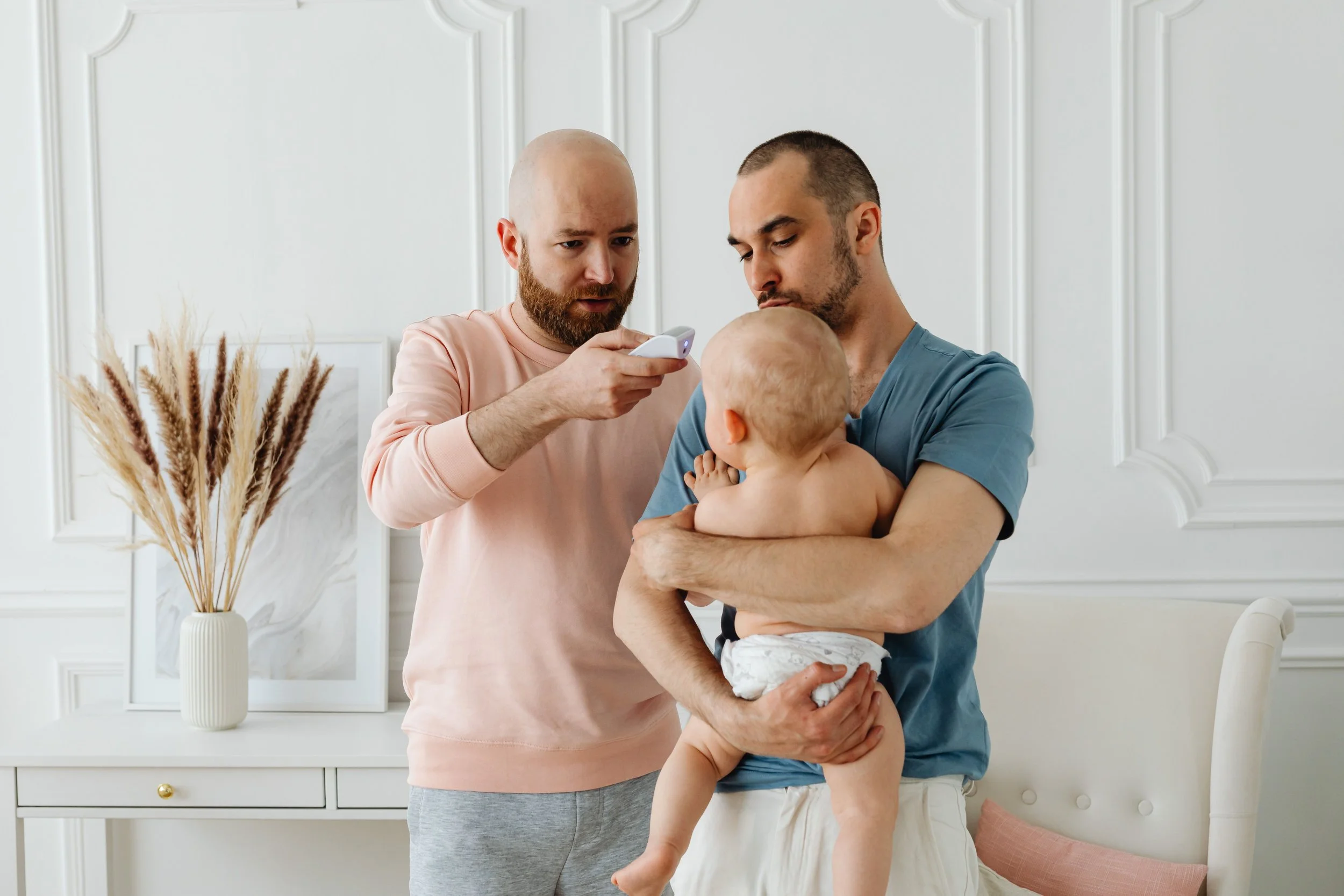 Two male parents taking temperature of their baby