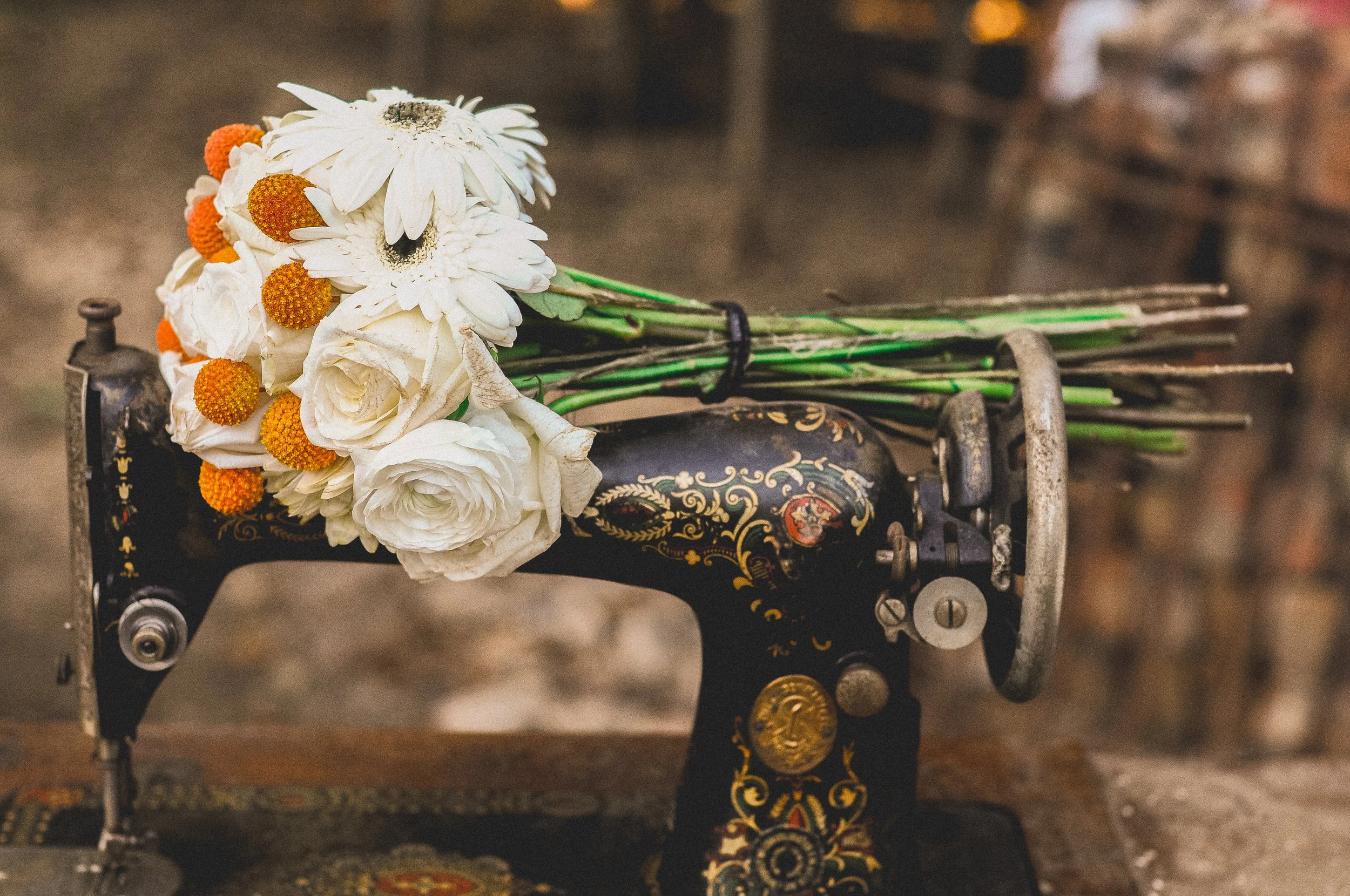 A bouquet of white daisies and orange flowers resting on an ornate vintage sewing machine.
