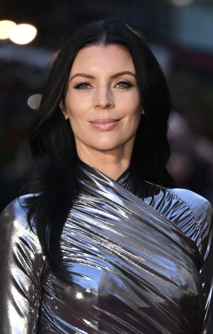 A woman with long black hair, wearing a shiny metallic silver top, smiling at the camera.