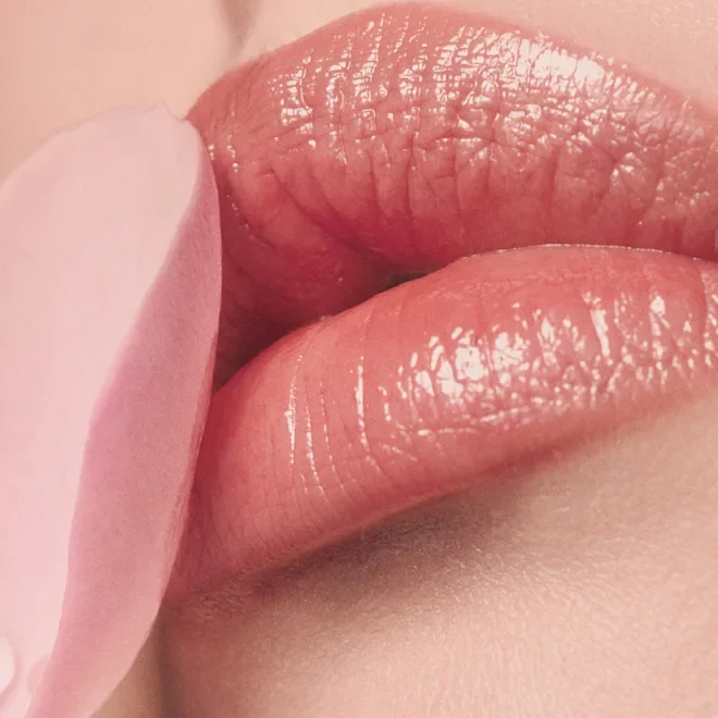 Close-up of glossy, nude-colored lips touching a pink finger.