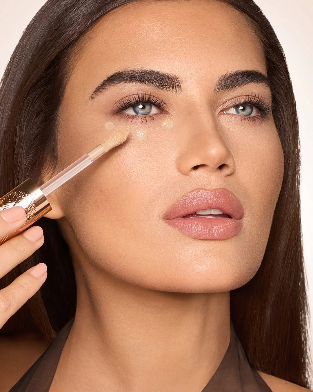 Close-up of a woman applying concealer under her eye with a brush.