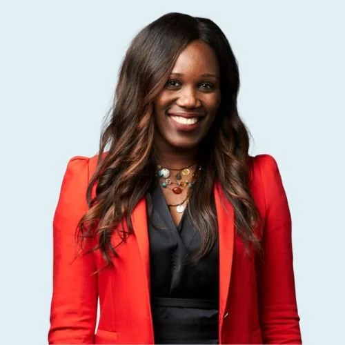 EBUN ONAGORUWA is wearing a red blazer over a black top and layered necklaces, smiling against a light blue background.