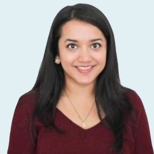 SWATI TEERDHALA is wearing a maroon top and silver jewelry, smiling at the camera against a light blue background.