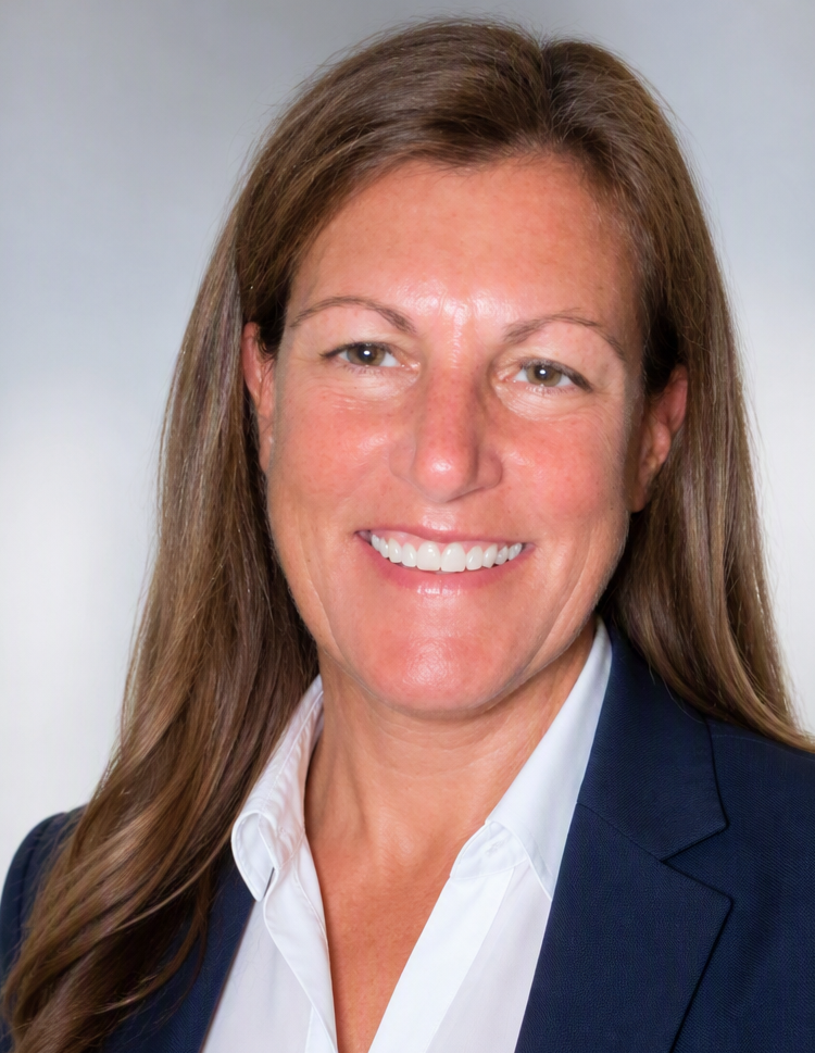 A woman with long brown hair, wearing a dark blazer and white shirt, smiling.