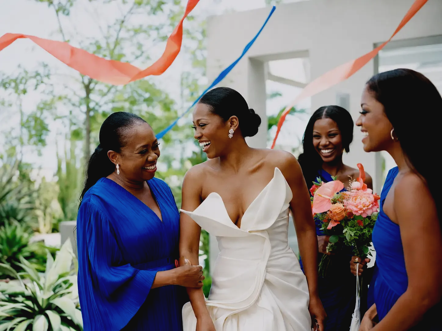 A bride celebrating outdoors with members of her wedding party beneath colorful streamers.