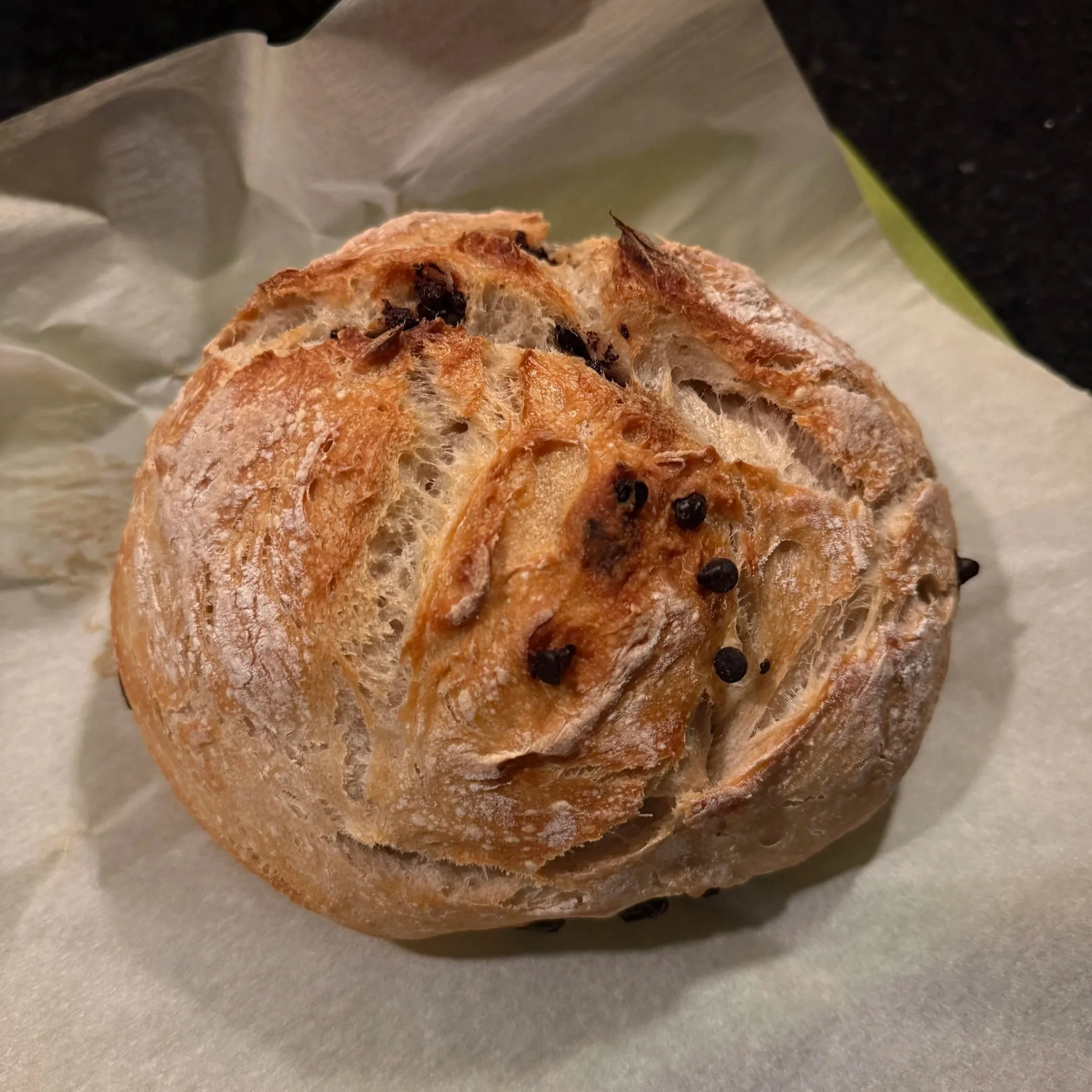 Freshly baked chocolate chip sourdough bread with a crisp golden crust, artisan scoring, and chocolate chips baked throughout the loaf