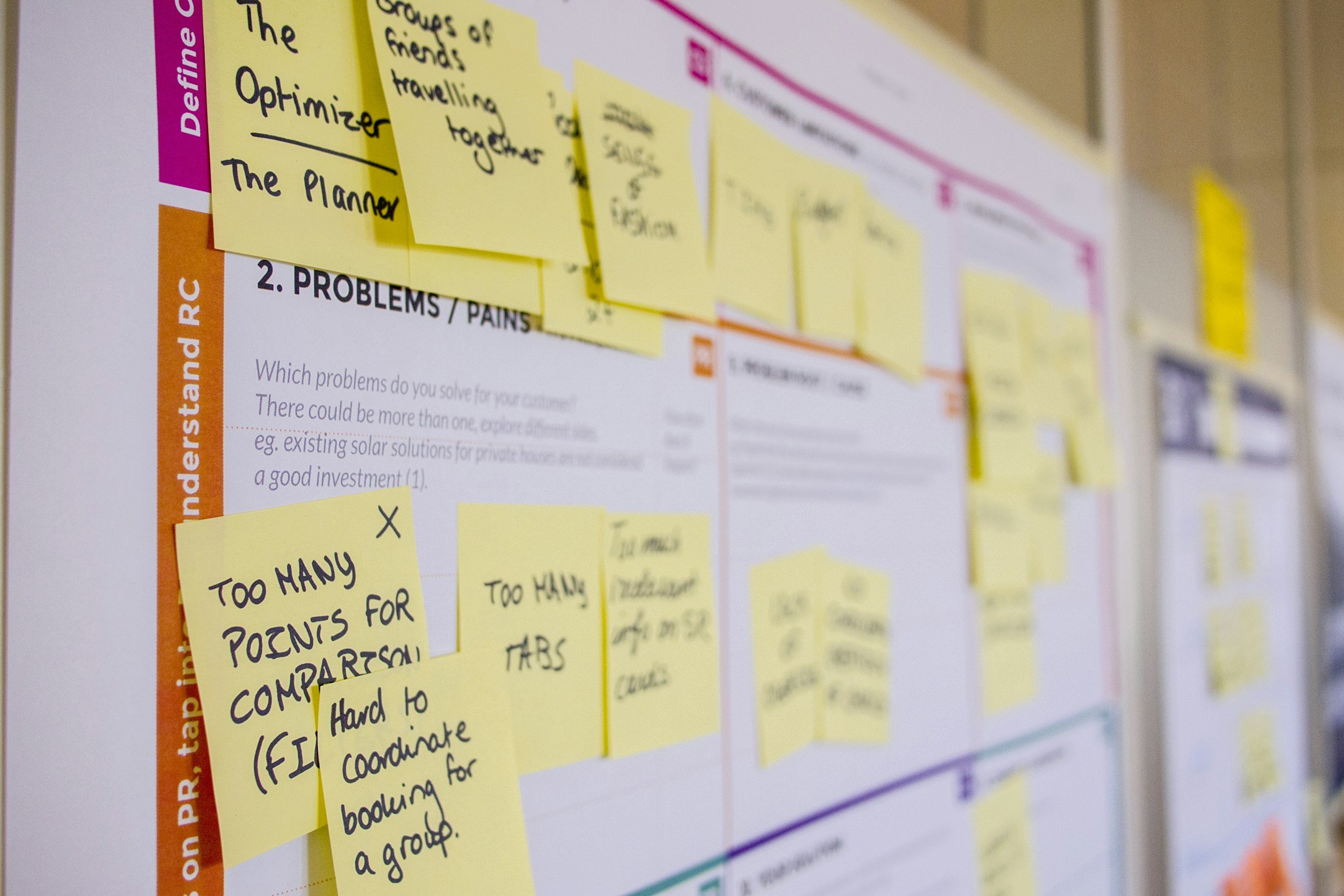 Close-up of a presentation board with several yellow sticky notes and some printed text, including a pink and orange sidebar. The notes contain handwritten messages, though some are partially obscured.