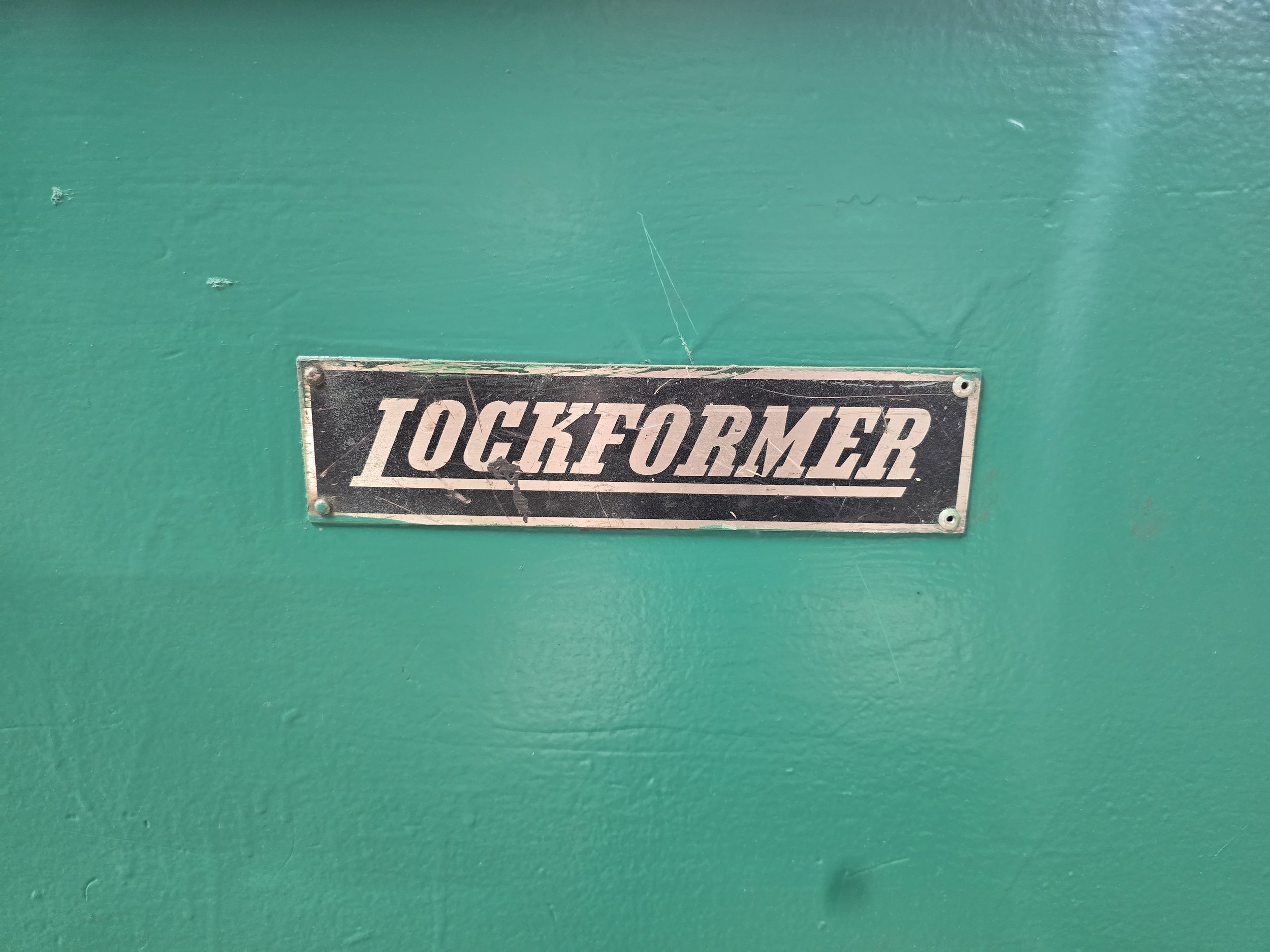 Close-up of a green object with a black and white metal label that reads 'TICKETOMETER' attached with four screws.