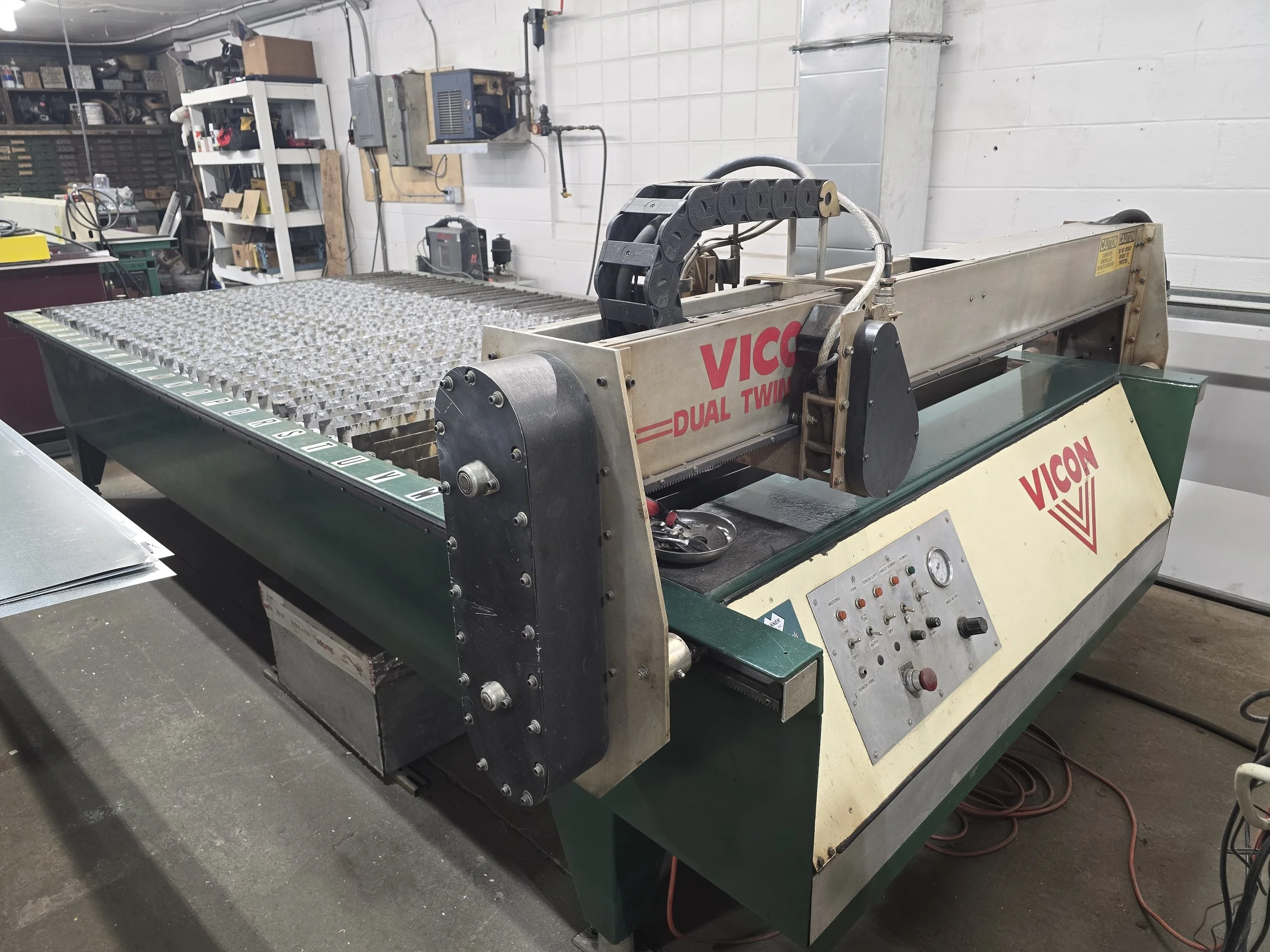 Plasma Cutter in a workshop with control panel, conveyor belt, and textured metallic surface, labeled 'VICON DUAL TWIN'.