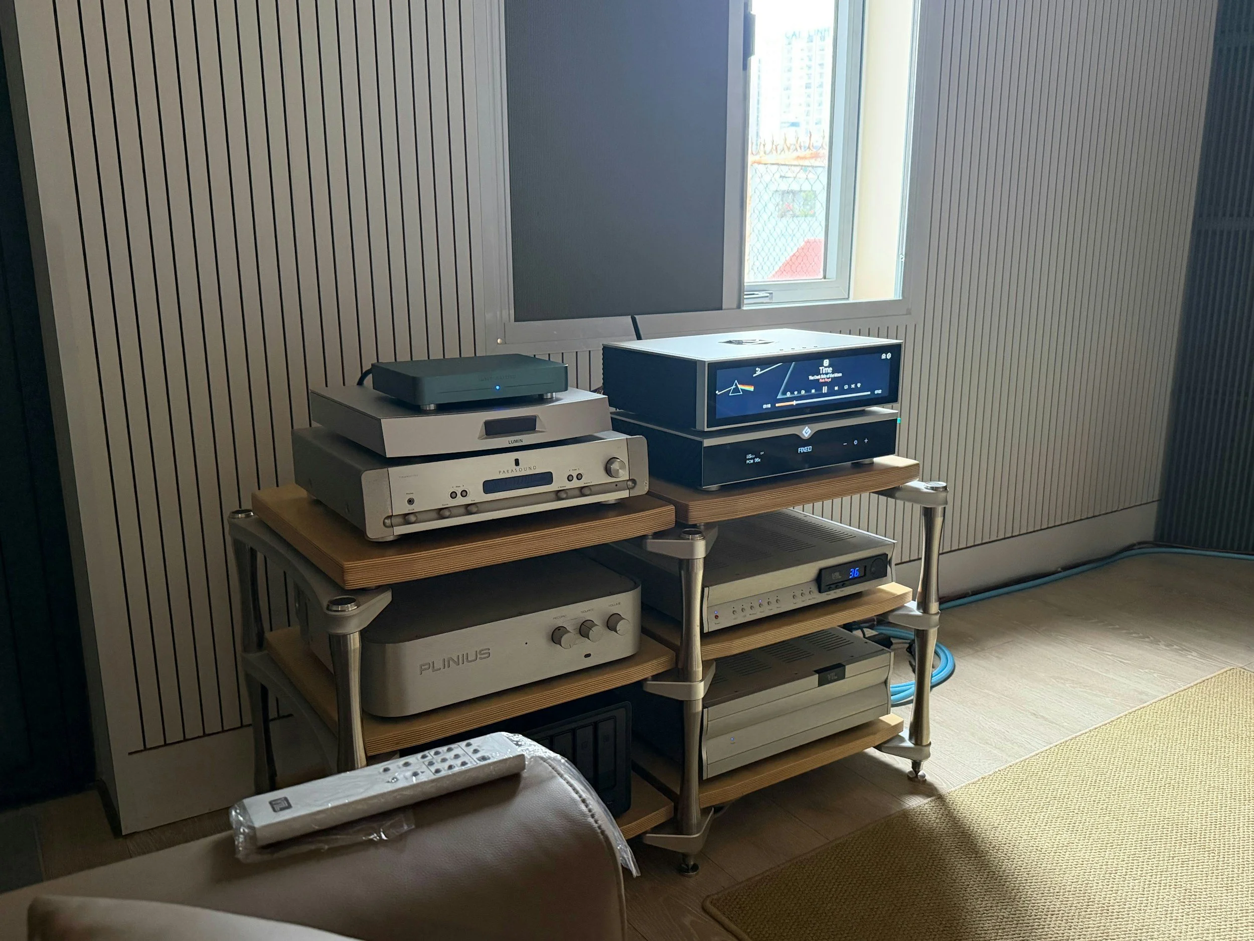 Music equipment on a wooden rack in a room with a window. Includes a turntable, audio receivers, and other electronic devices.