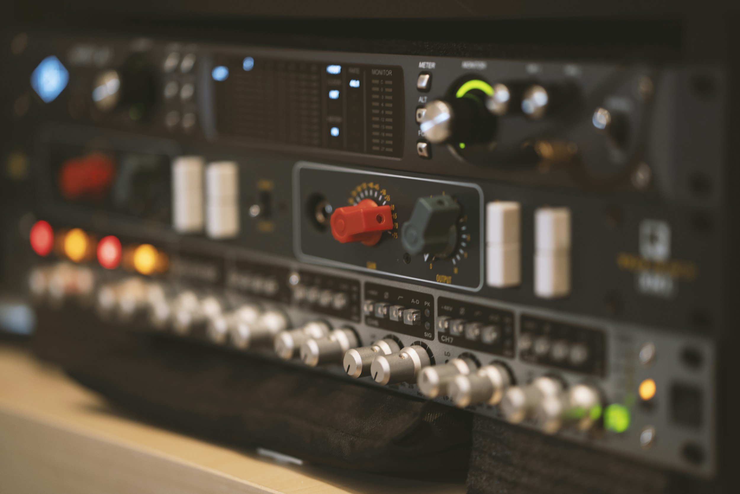 Close-up of a professional audio mixing or recording equipment with various buttons, knobs, and meters illuminated with blue and green lights.
