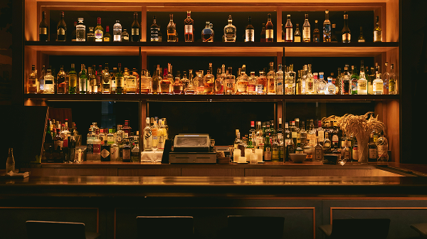 Bar with bottles of various alcoholic drinks displayed on illuminated shelves behind the counter