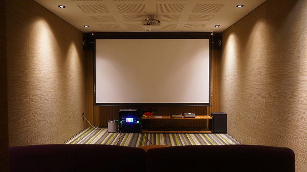 Home theater room with a large projector screen, speakers, and media equipment on the floor.