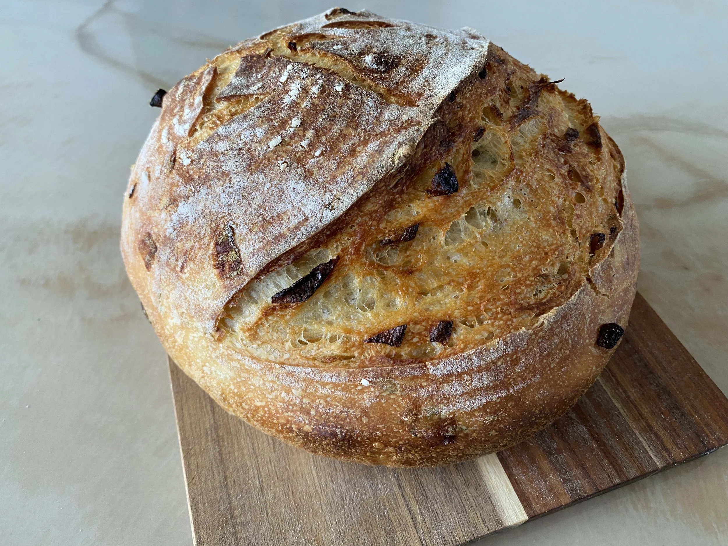 Close-up of a freshly baked round bread with a crispy crust, dusted with flour, resting on a wooden cutting board.