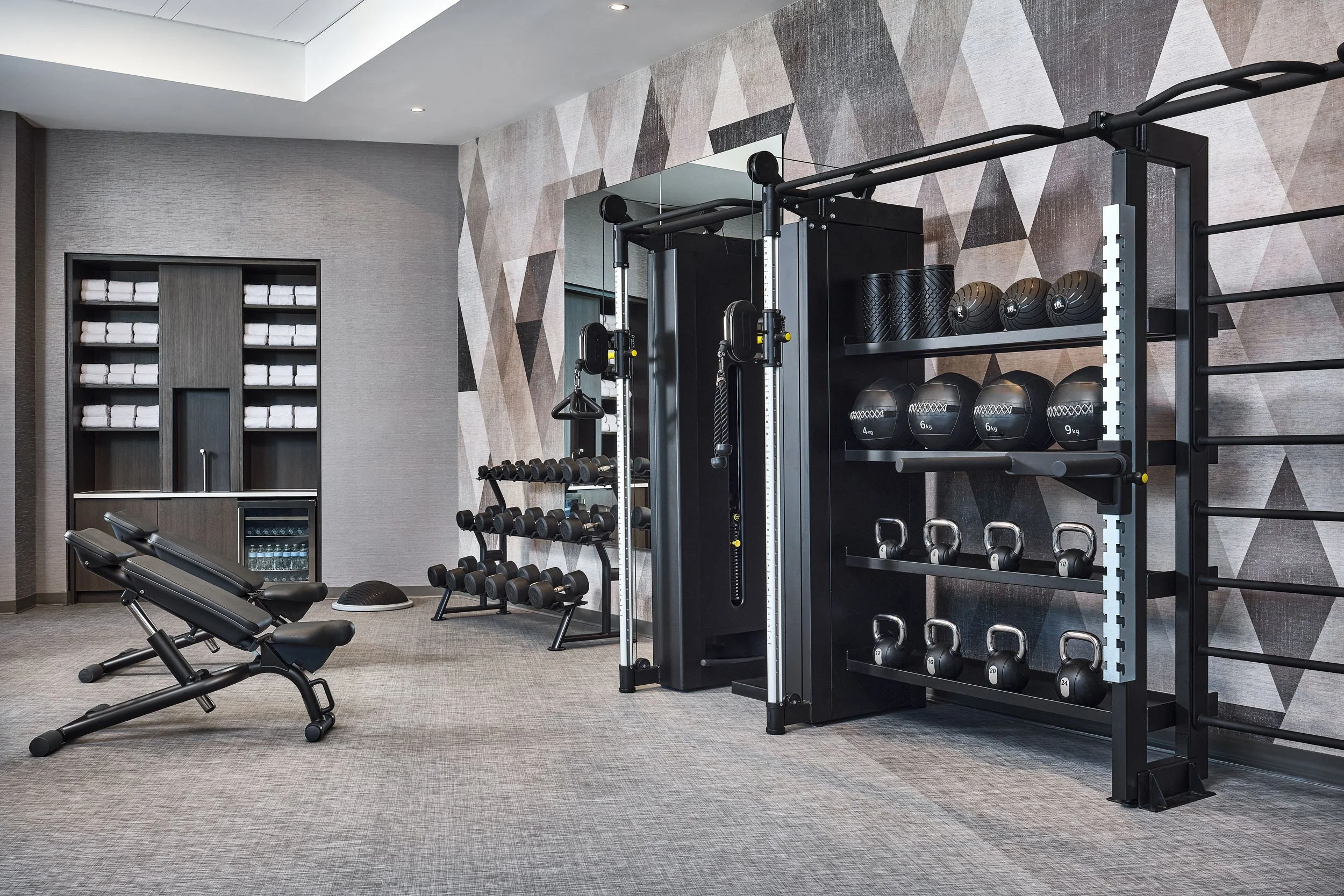 Modern gym with workout equipment including a weight rack, dumbbells, exercise balls, a workout bench, and a mirror on the wall.