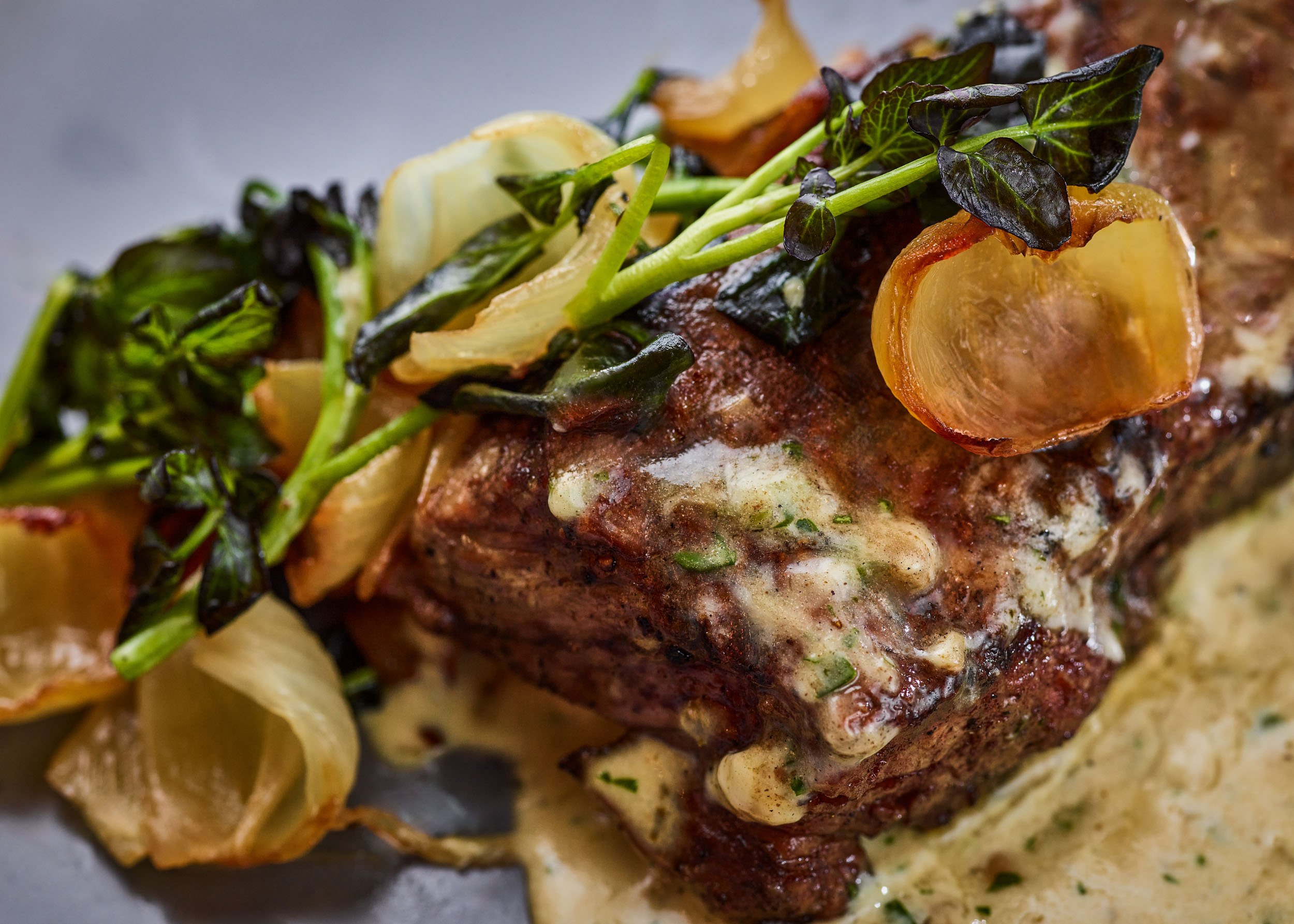 Close-up of a cooked dish featuring a piece of beef topped with herbs and caramelized onions, served with roasted potatoes.