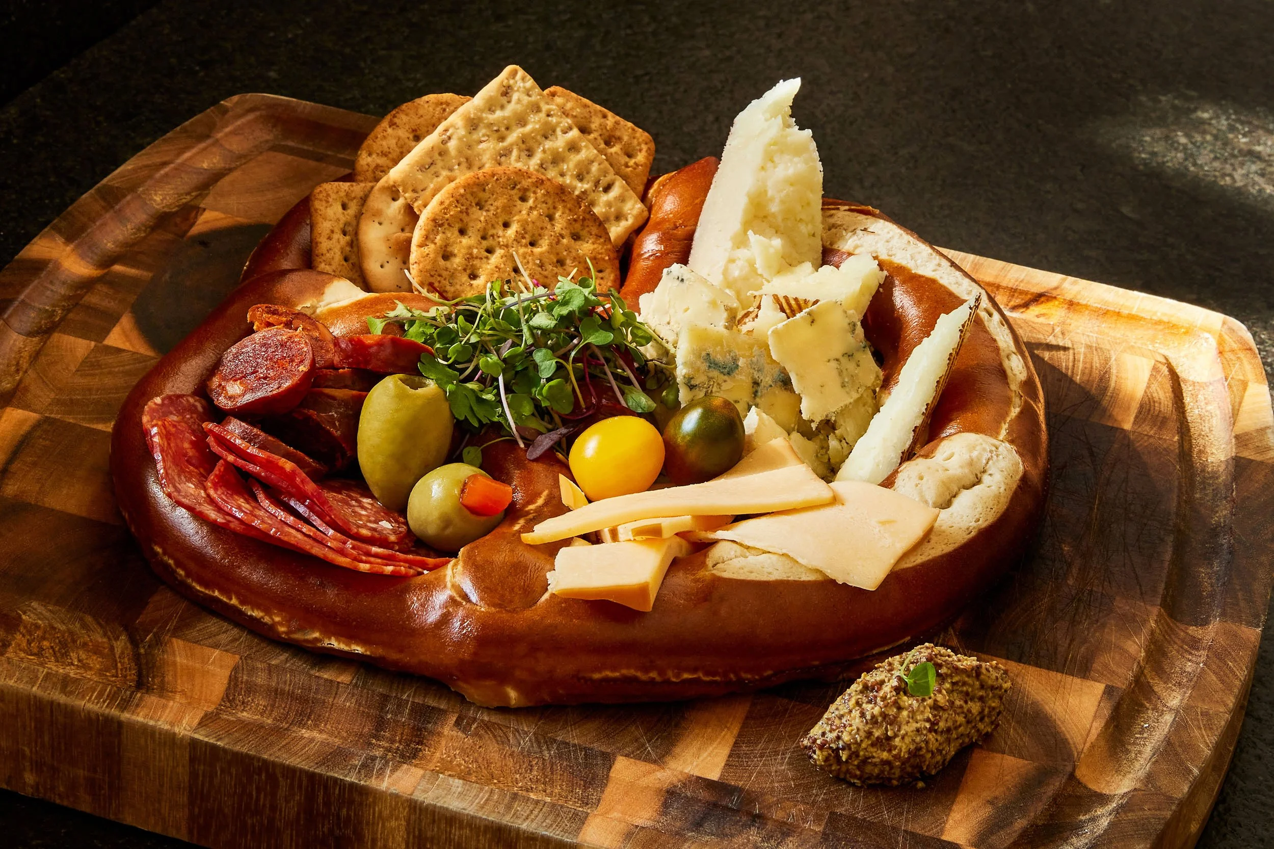 Cheese, crackers, cured meats, grapes, microgreens, and a spread on a wooden serving platter.