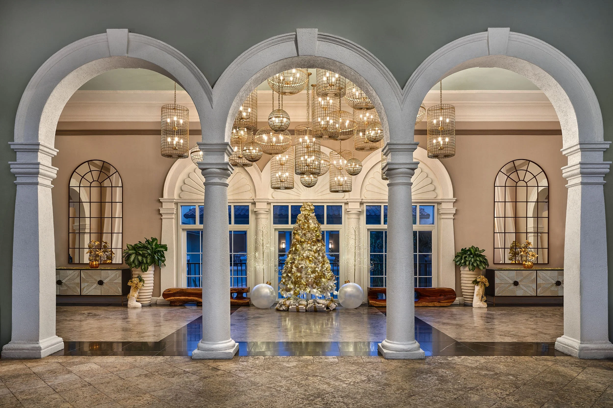 Elegant interior with white arches, a decorated Christmas tree, modern chandelier, large windows, and festive decor.