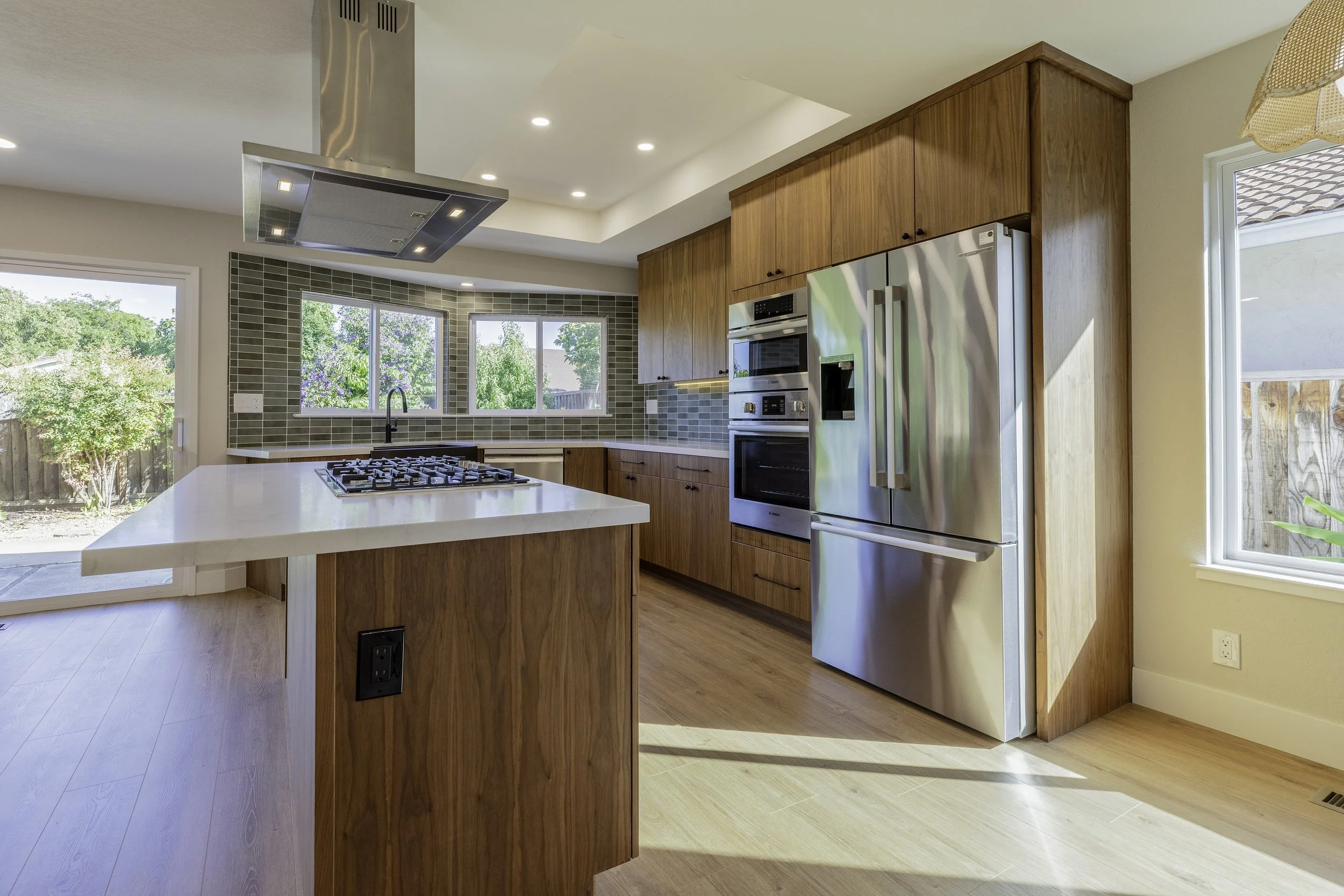 Kitchen with wooden cabinets, stainless steel refrigerator, built-in oven, large windows, and a kitchen island.