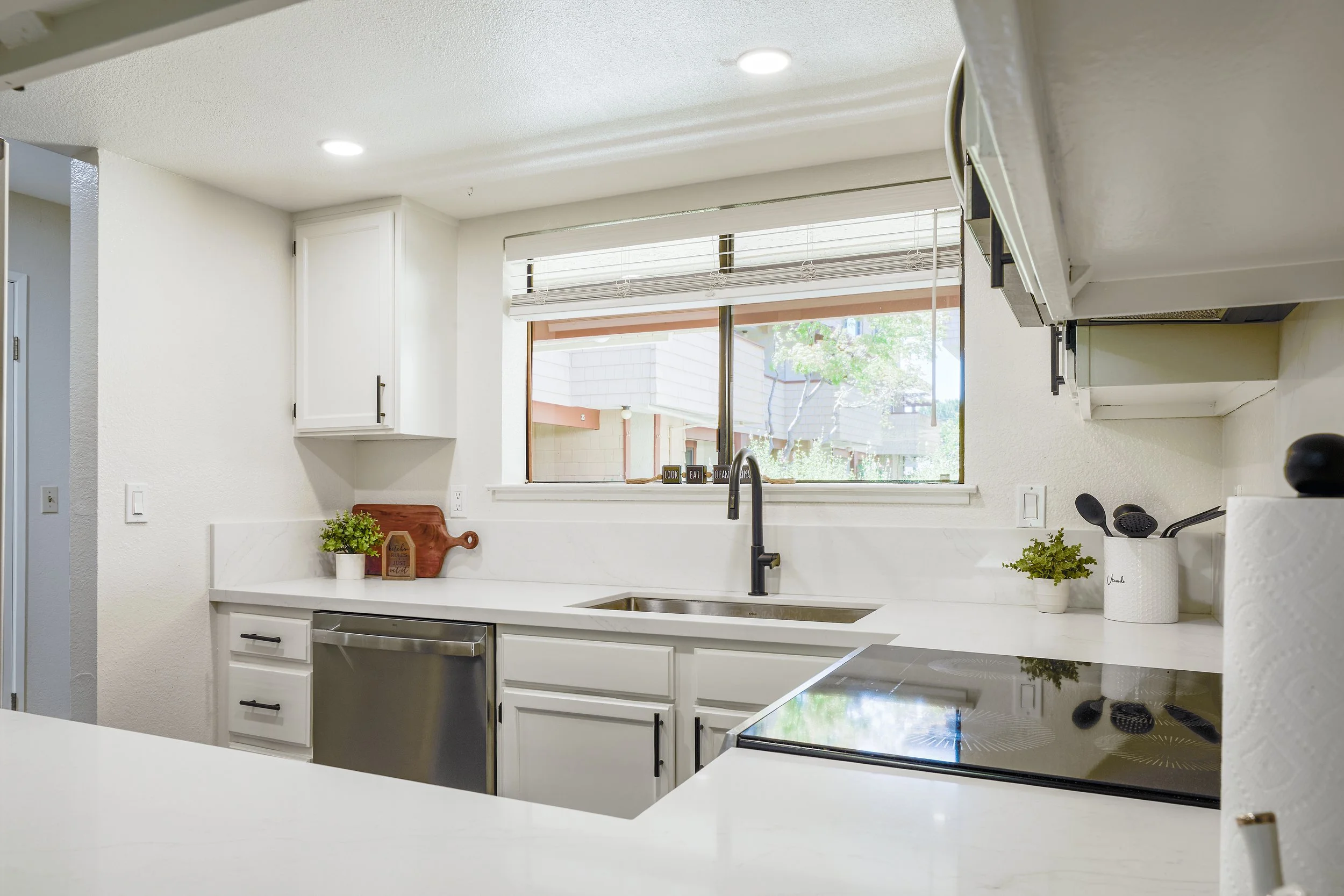 Kitchen with white cabinets, a window with blinds, a countertop with plants, and modern appliances.