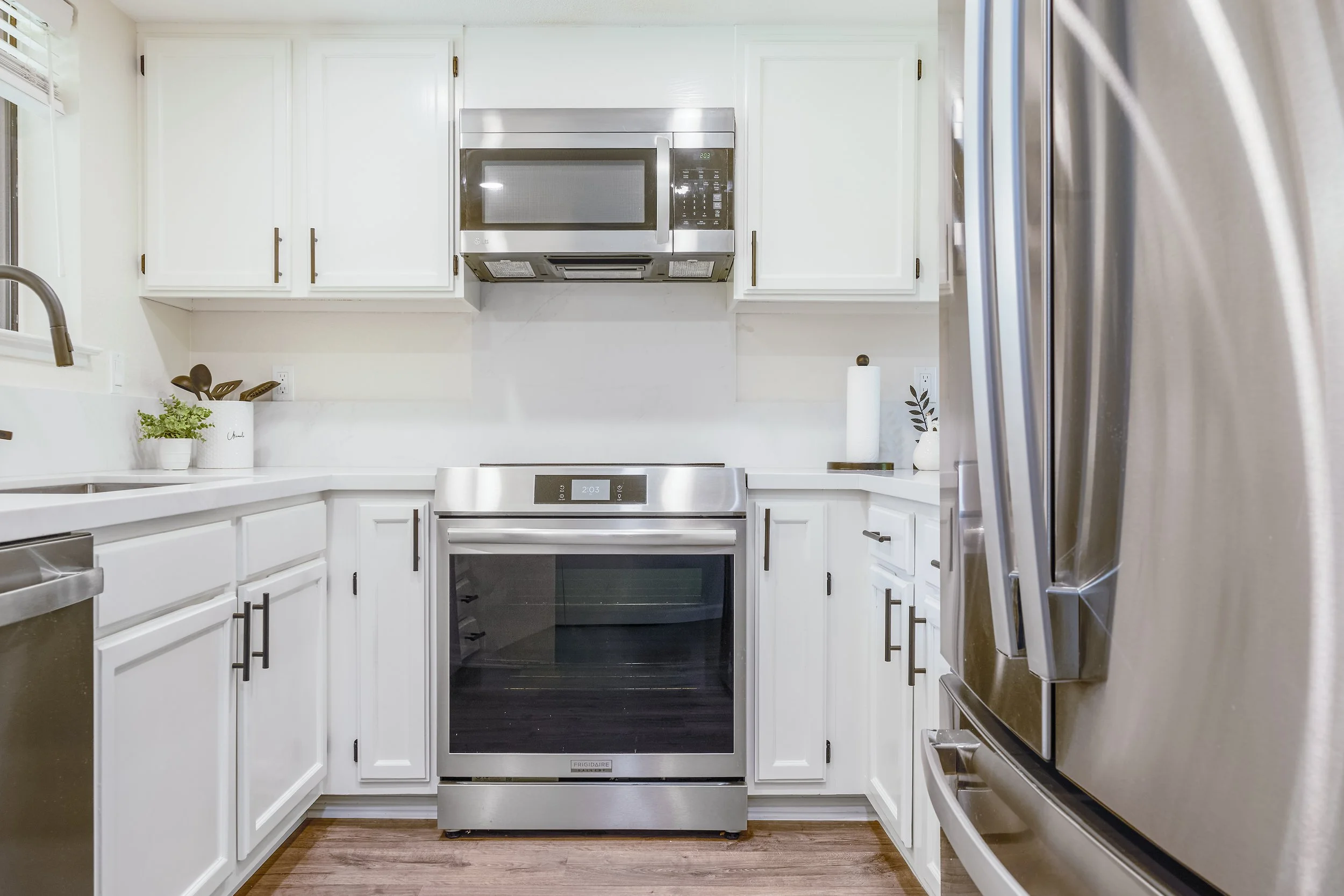 Kitchen with white cabinets, stainless steel microwave and oven, and a side view of a stainless steel refrigerator.
