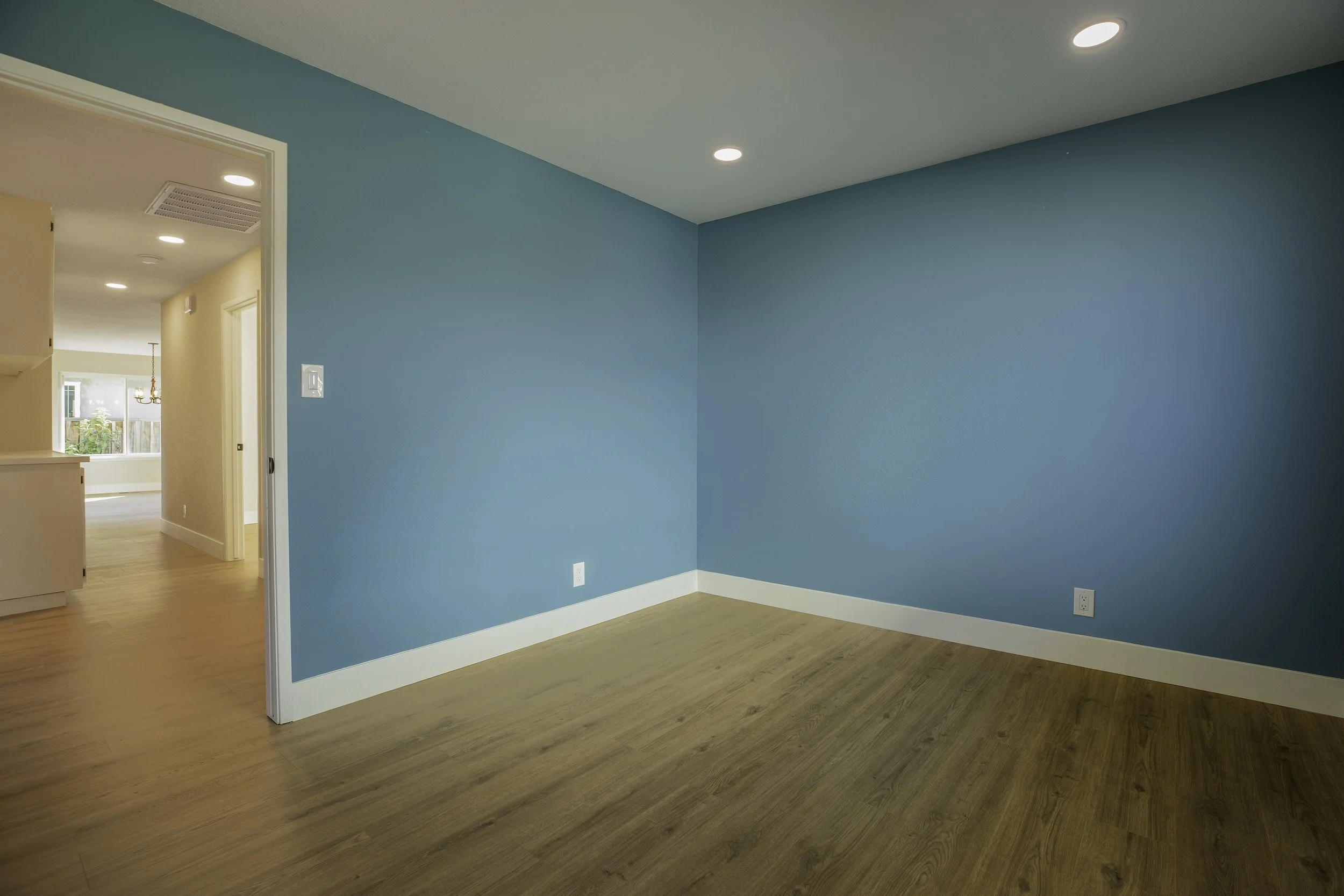 Empty room with turquoise walls, wood flooring, and recessed ceiling lights.