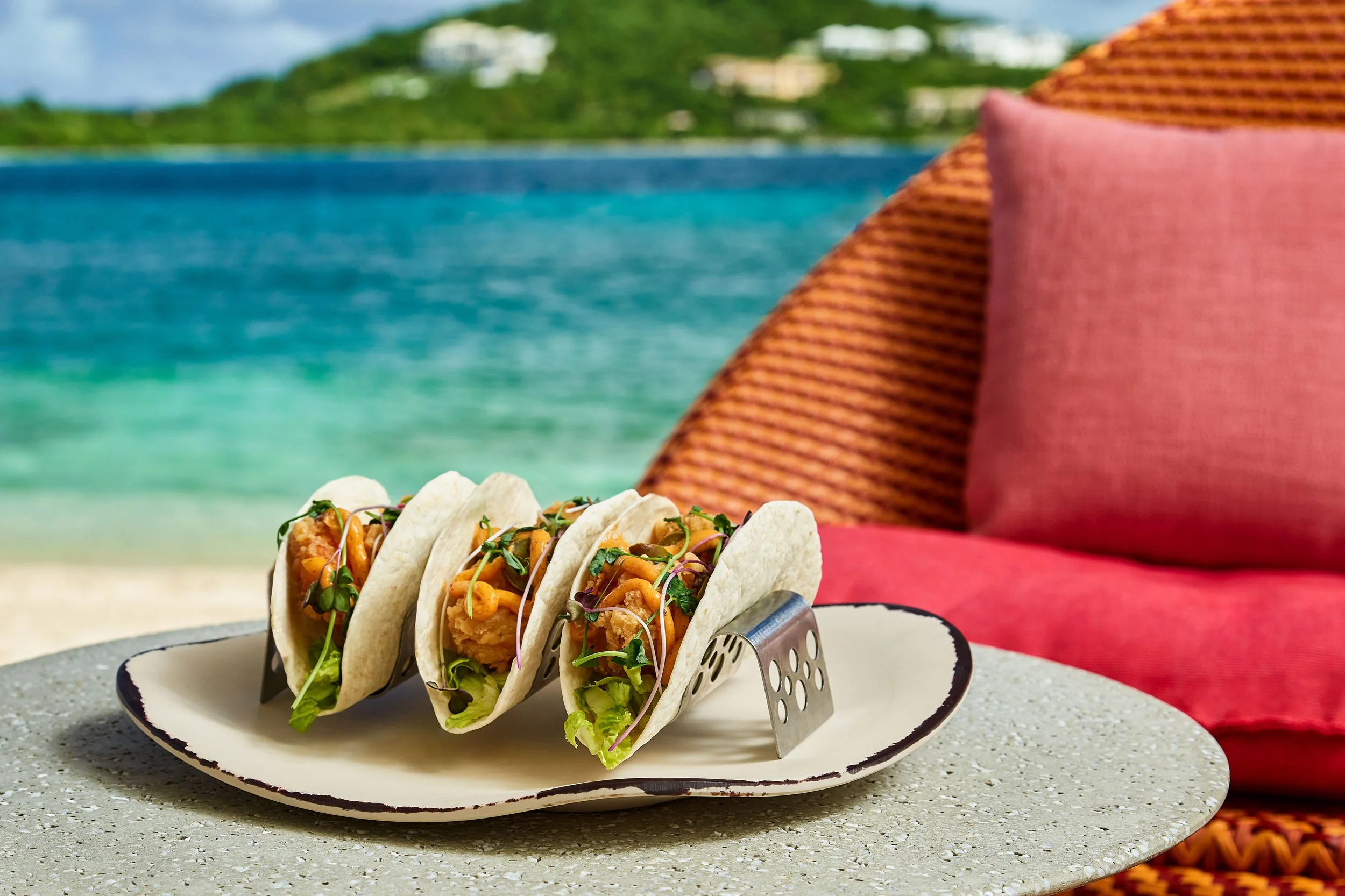 Three tacos filled with fried fish, shredded lettuce, and microgreens on a white plate.
