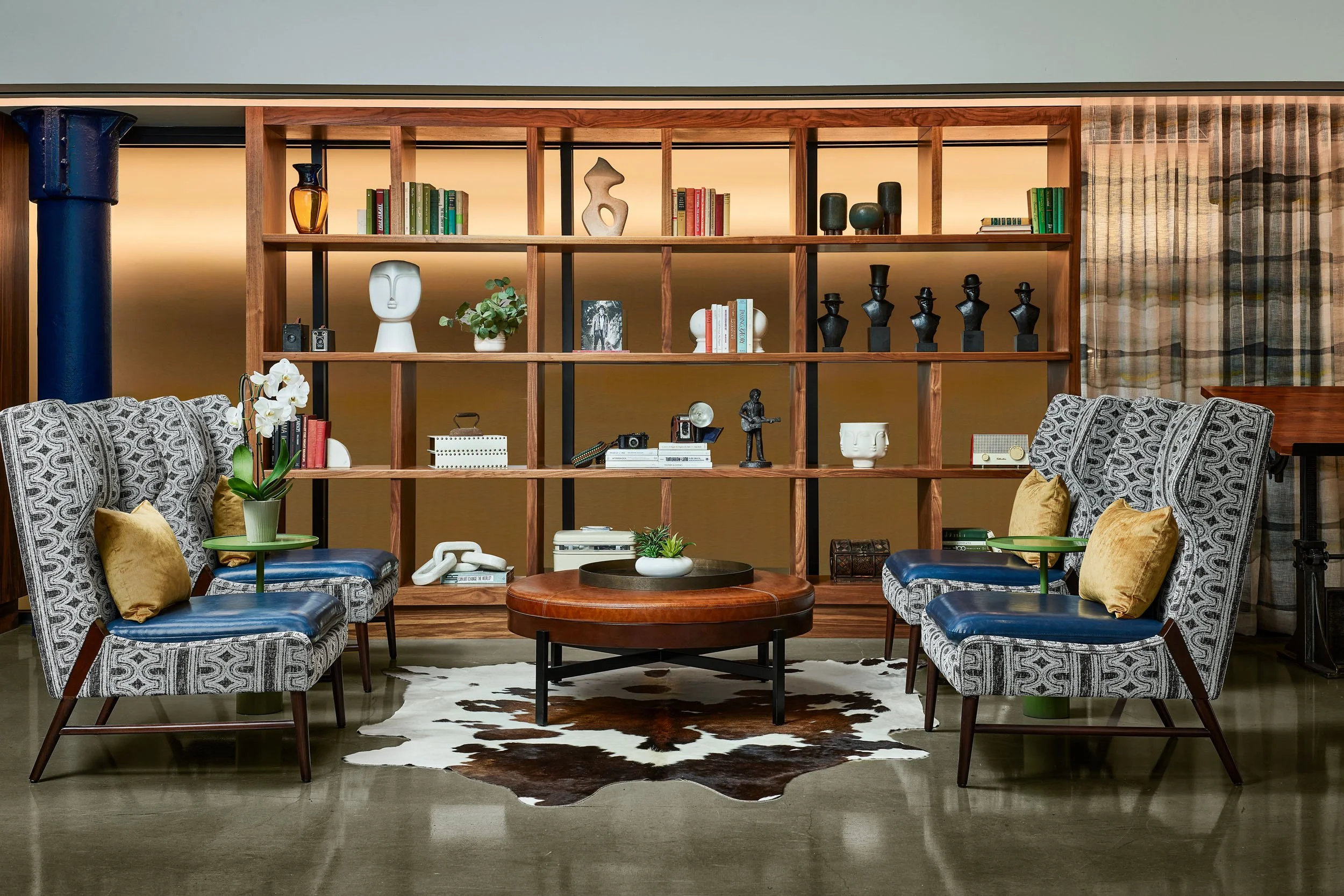 Living room with patterned armchairs, a wooden coffee table, a cowhide rug, and a large wooden bookshelf filled with books and decorative objects.