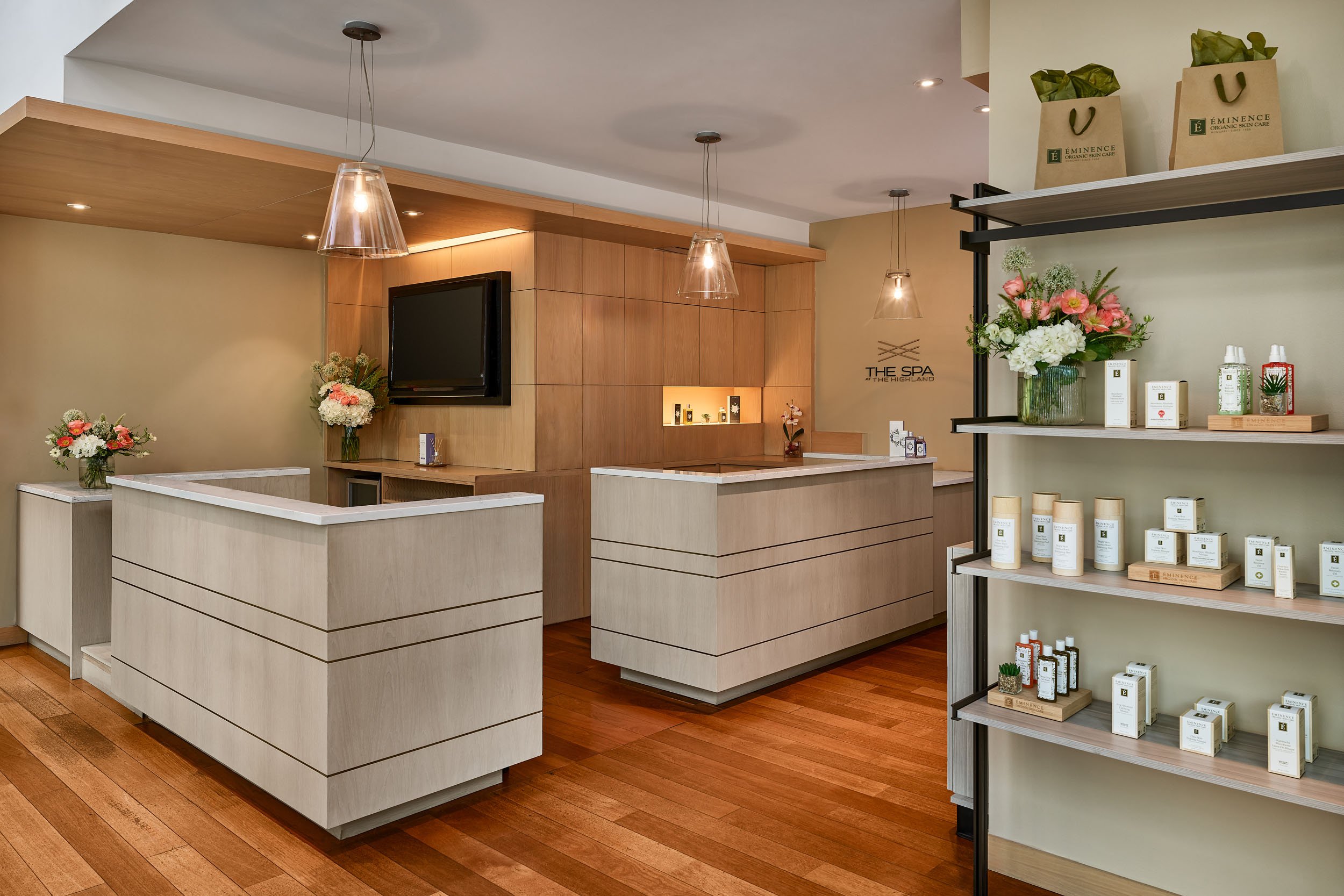 Interior of a spa reception area with white and wooden counters, floral arrangements, product shelves, and pendant lights.