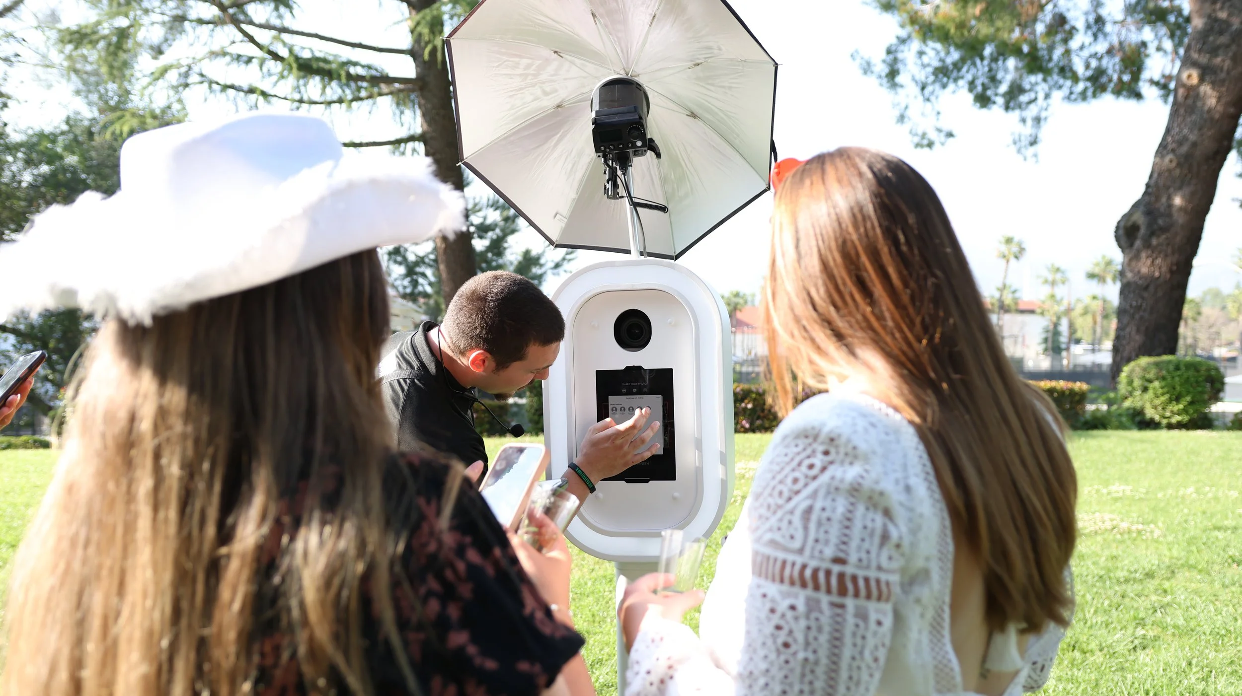 Guests gathered around a white digital photo booth at an outdoor event.