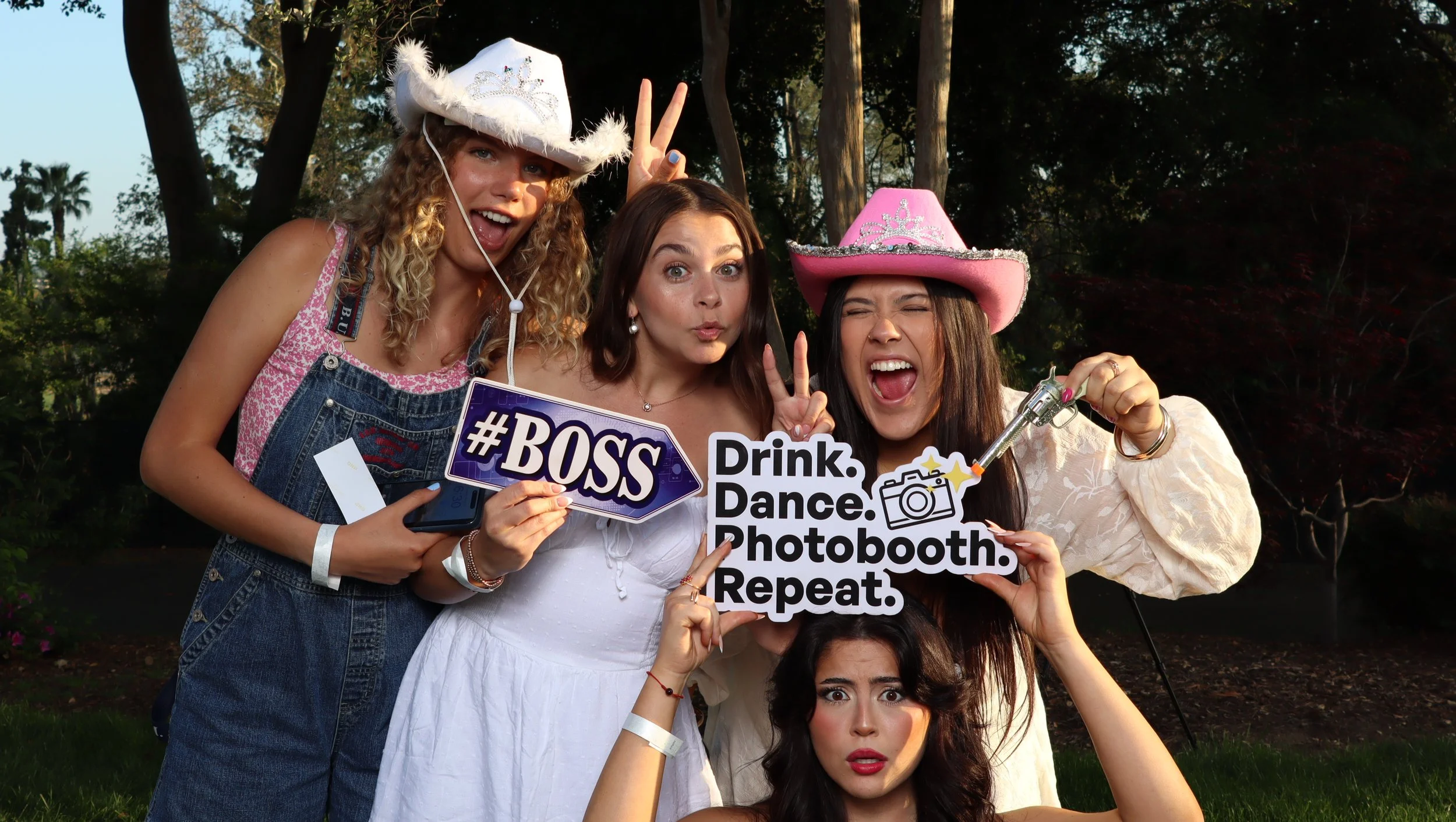 Four women posing with cowboy hats and signs at an outdoor photo booth.