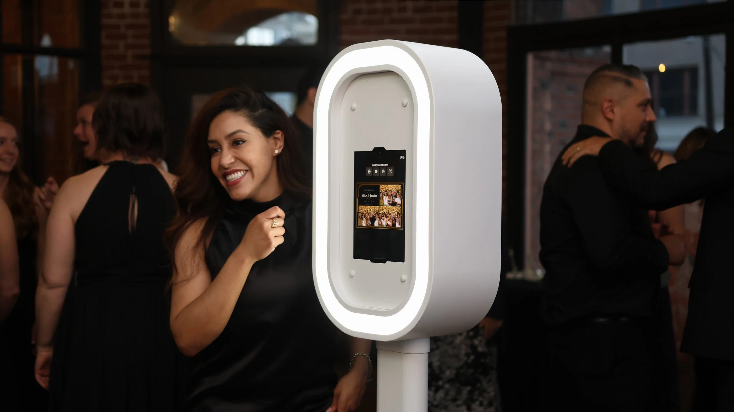 Woman smiling beside a white digital photo booth at an indoor event.