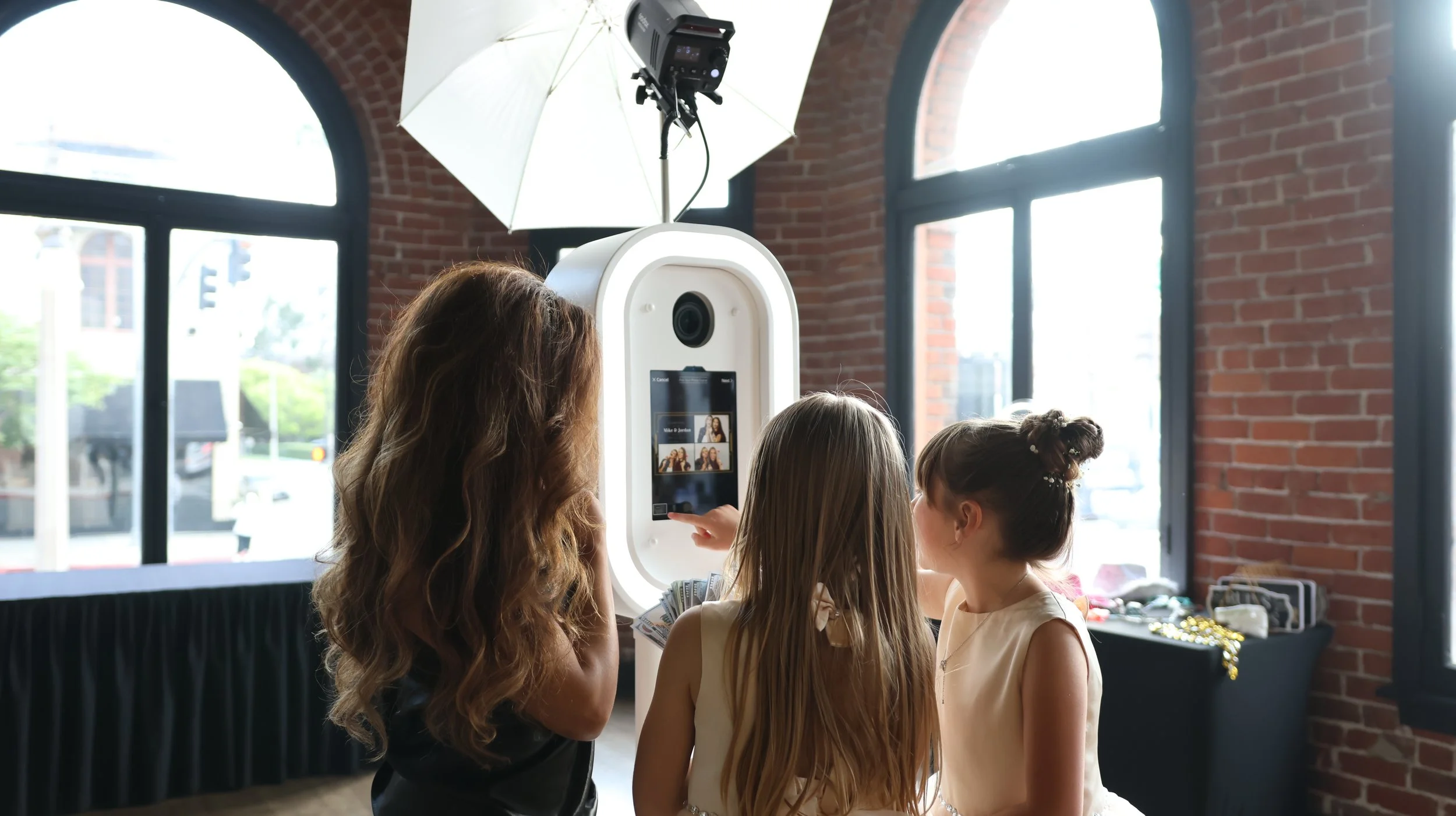 Three guests using a white digital photo booth inside an event venue.