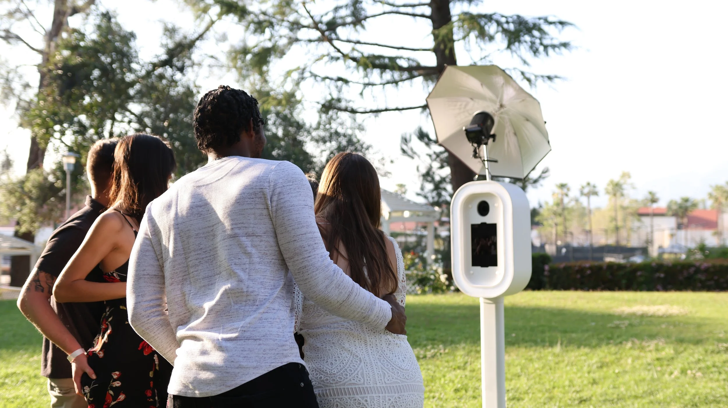 Couple standing beside a white digital photo booth at an outdoor event.