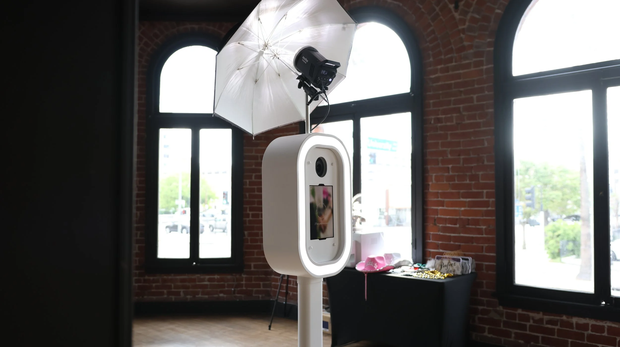 White digital photo booth set up inside an event venue with exposed brick walls and large windows.