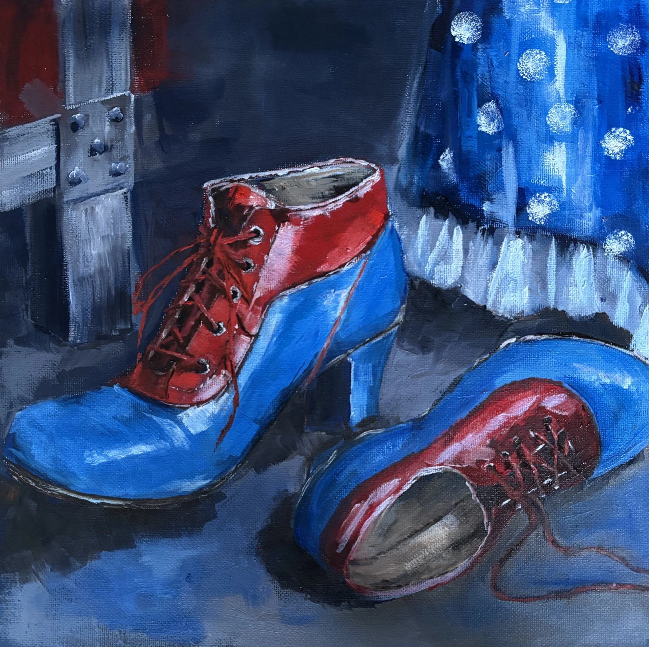 Painting of blue and red heeled boots, one upright and one lying on its side, beside a blue polka-dot costume and a theatrical trunk.
