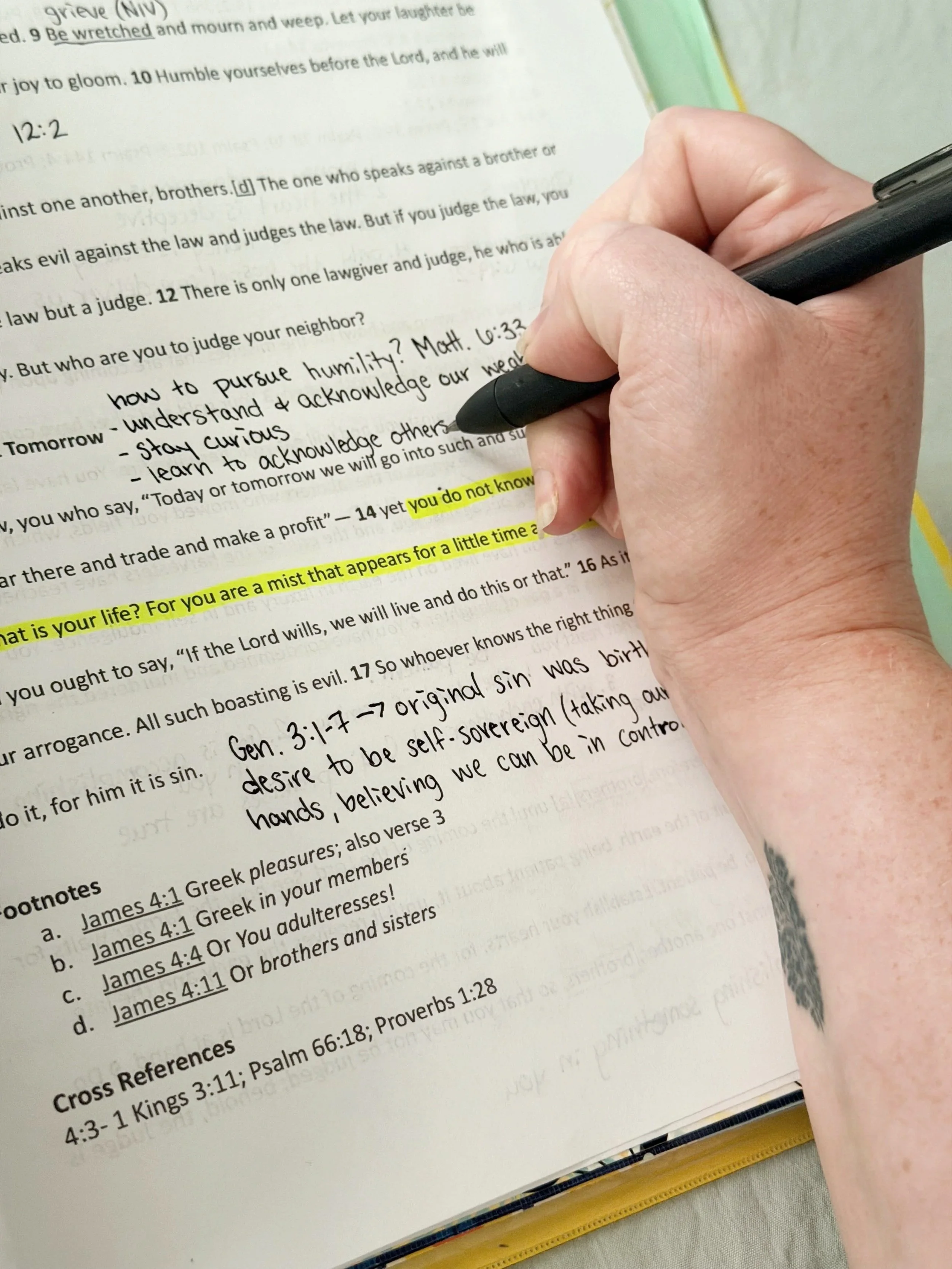 Close-up view of a person writing notes with a black pen on a printed page of text, with some sentences highlighted in yellow.