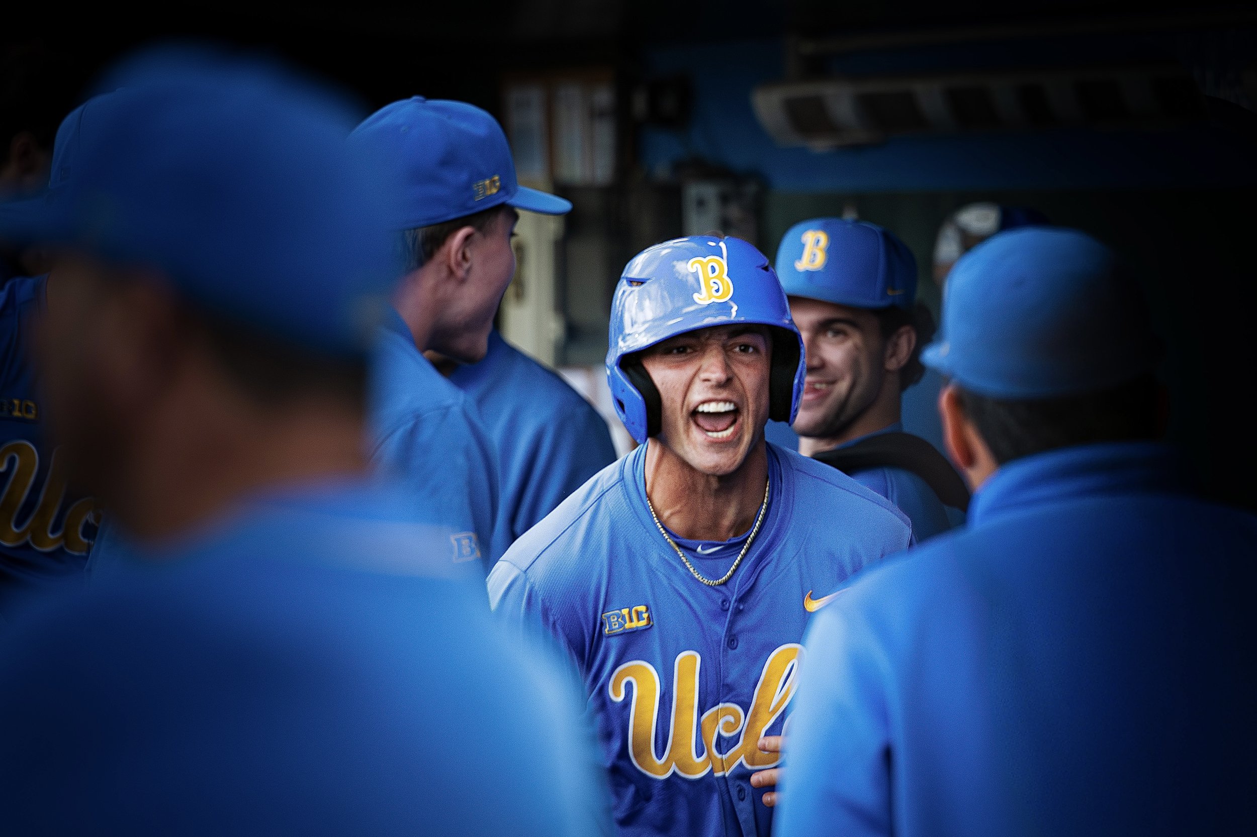 A group of baseball players wearing blue uniforms and helmets, gathered together in a dugout, with one player in the center shouting or talking passionately.