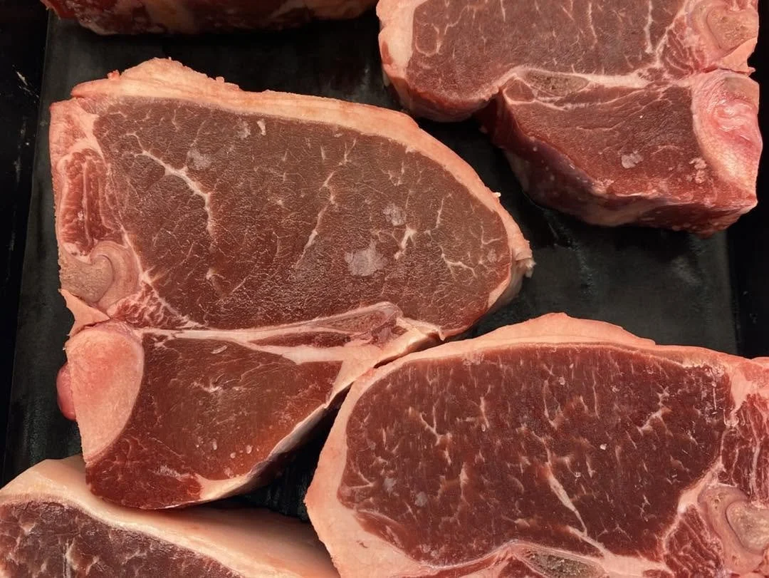 Various raw beef steaks on a black surface, showing marbling and thick cuts from Andy's Market.