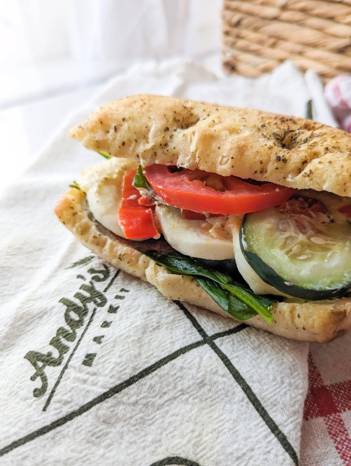 Andy's Market sandwich filled with sliced tomatoes, cucumbers, and greens, on a paper wrapper.