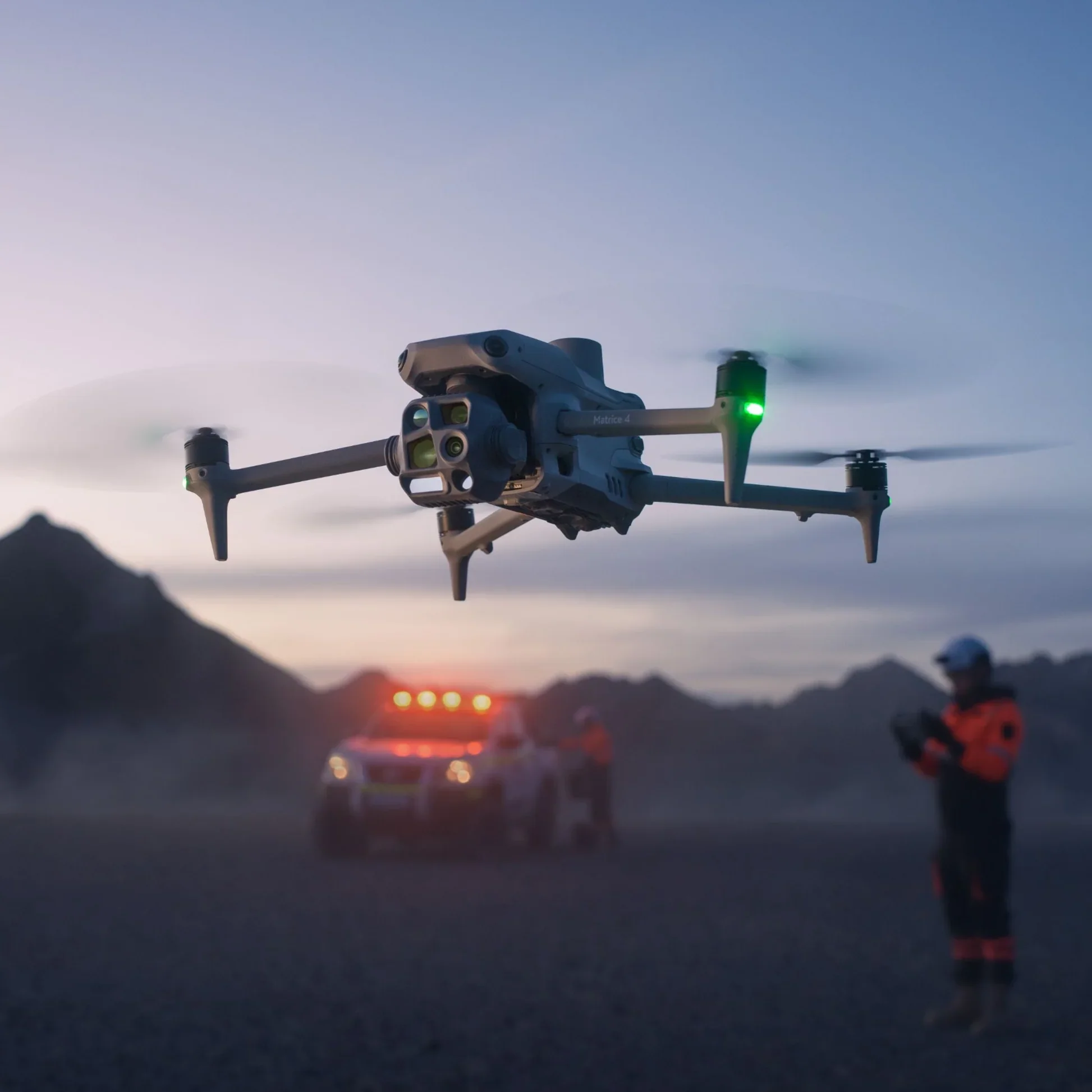 A drone with four propellers flying in the sky during sunset, with mountains in the background.