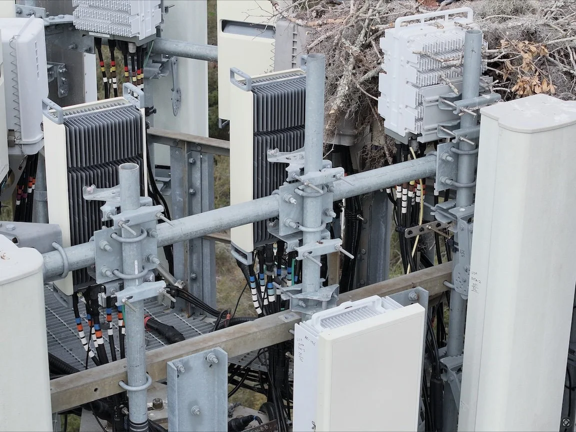 Close-up of electrical equipment with metal framework, cooling fins, and assorted wiring and components, outdoors.