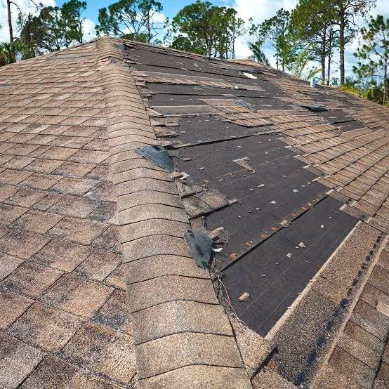 The roof has damaged and missing shingles, with some roofing materials peeled back or broken, indicating roof deterioration or repair work needed.