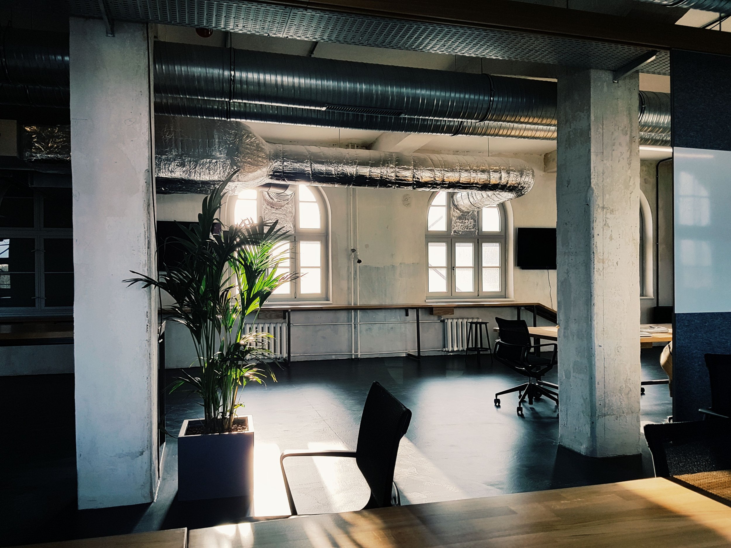 An industrial-style interior with exposed ductwork, large windows, and a mix of modern and rustic furnishings.
